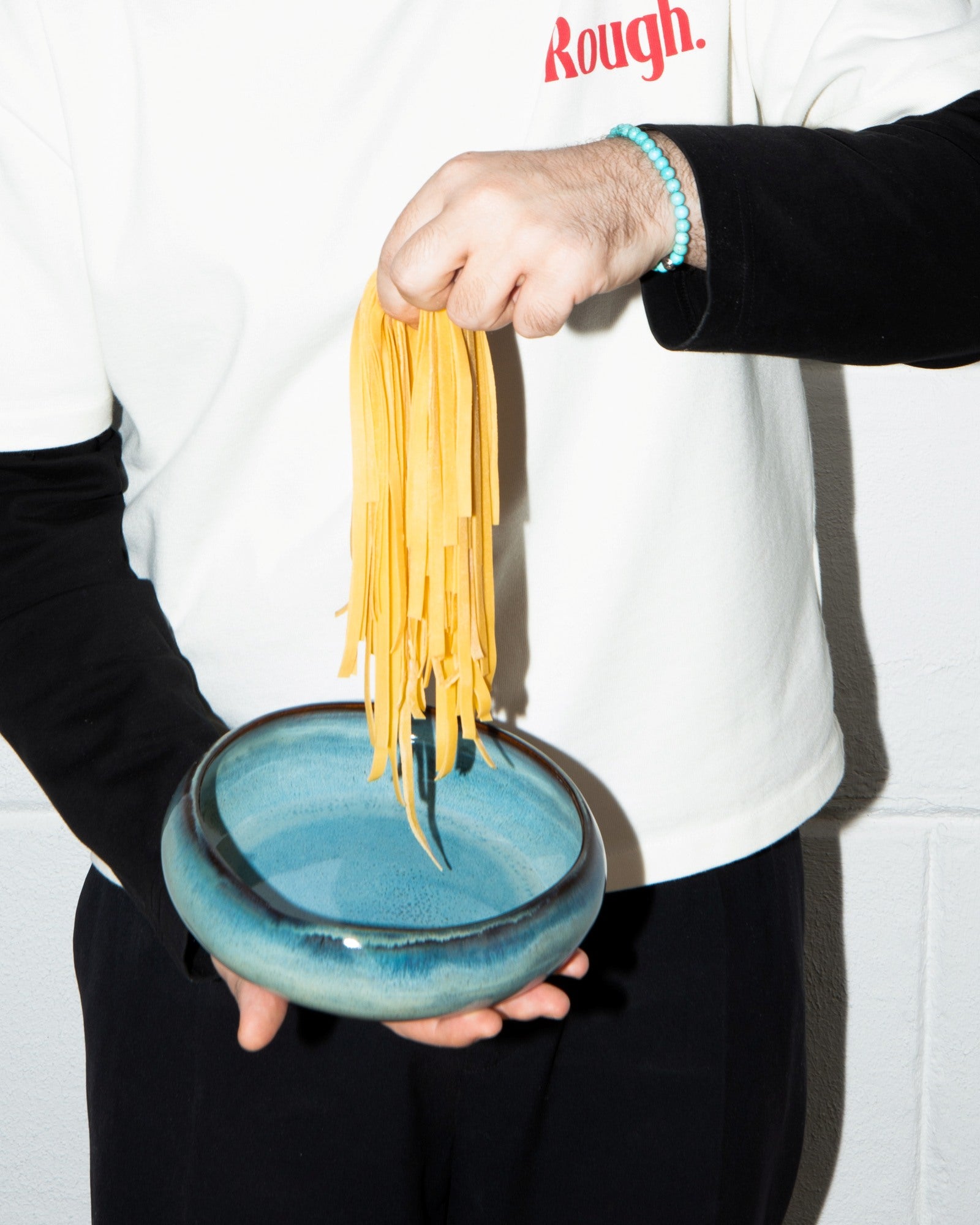 Eine Person hält eine blaue Schale und lässt gelbe Nudeln in sie hineinhängen.