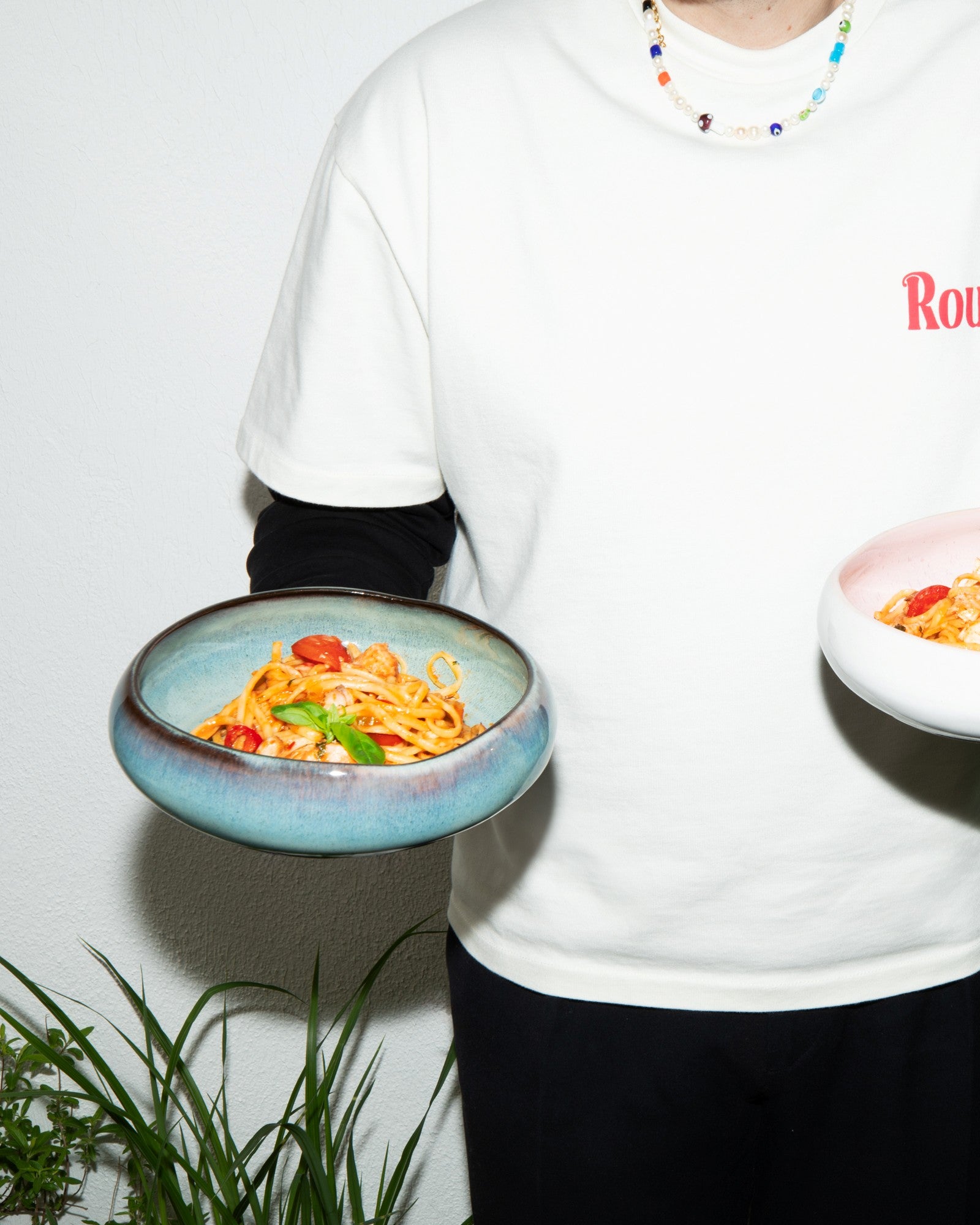Eine Person in weißem T-Shirt hält zwei Schüsseln mit Spaghetti.
