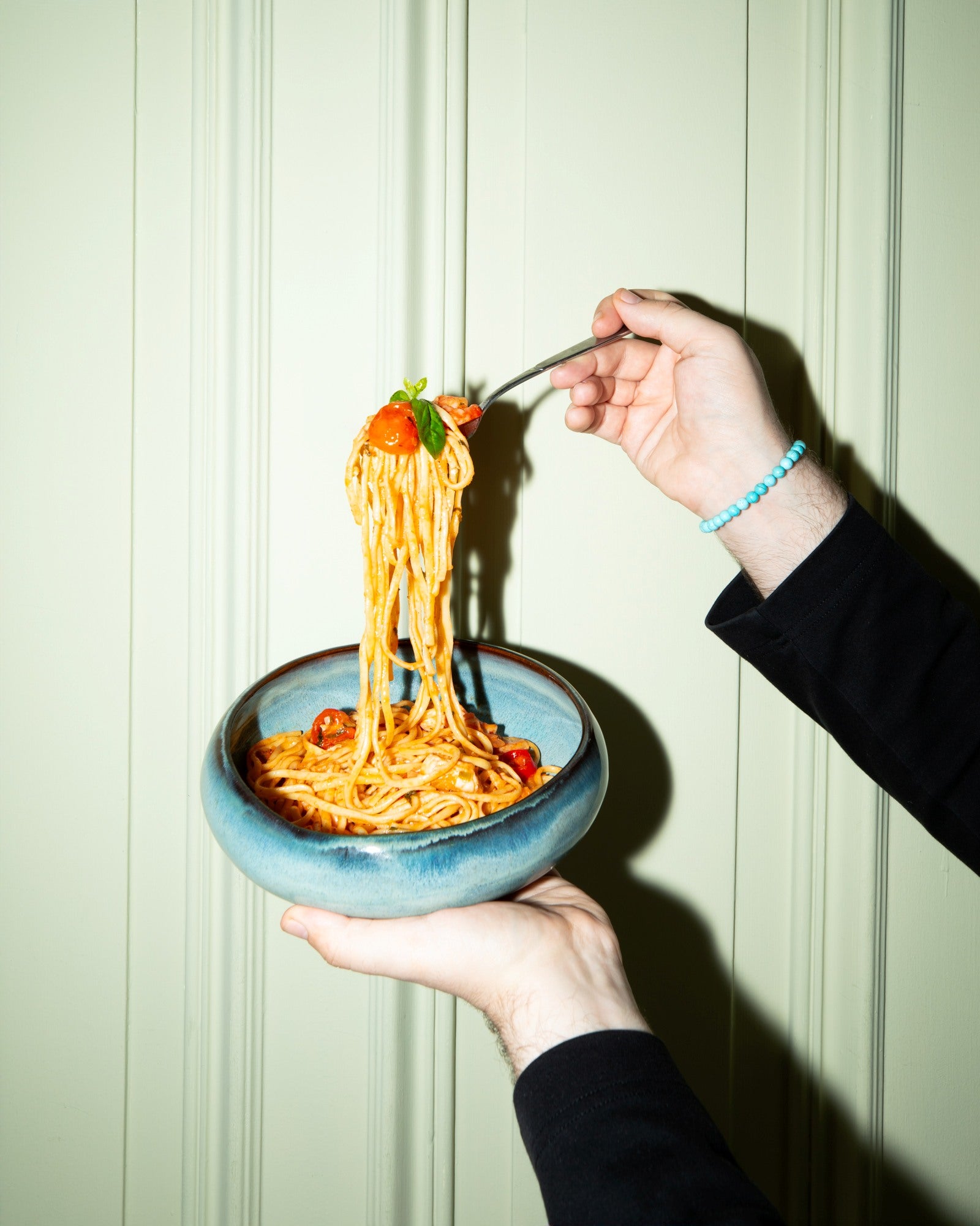 Eine Person hebt mit einer Gabel Spaghetti mit Tomaten aus einer blauen Schüssel.