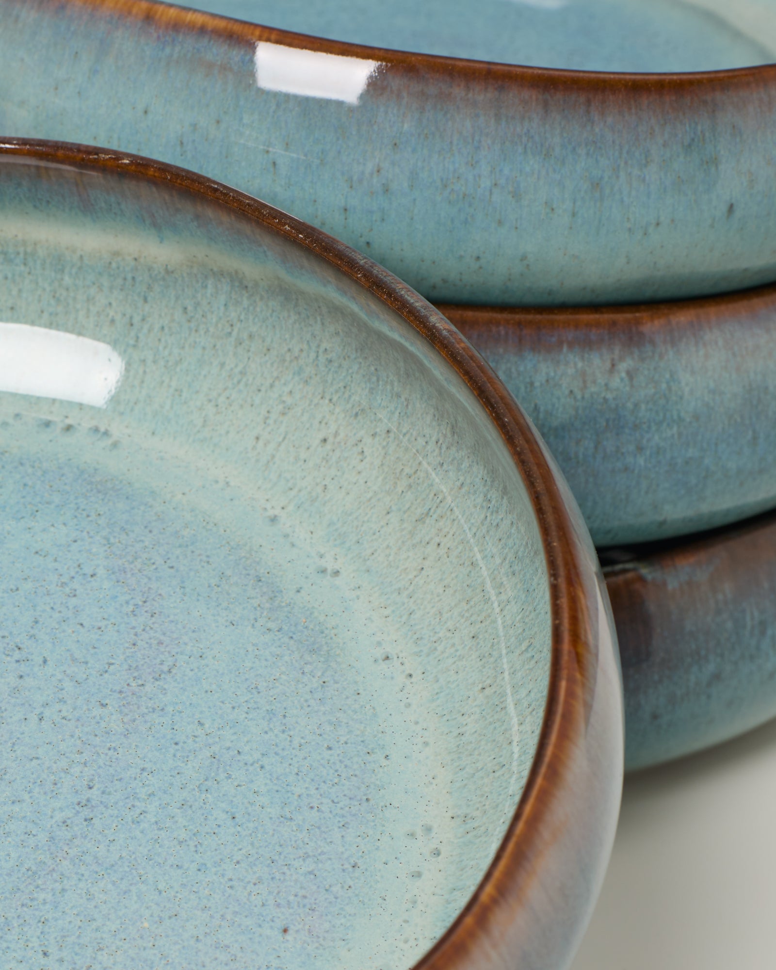 Nahaufnahme von drei stapelbaren Keramiktellern mit blauer Glasur und braunem Rand.