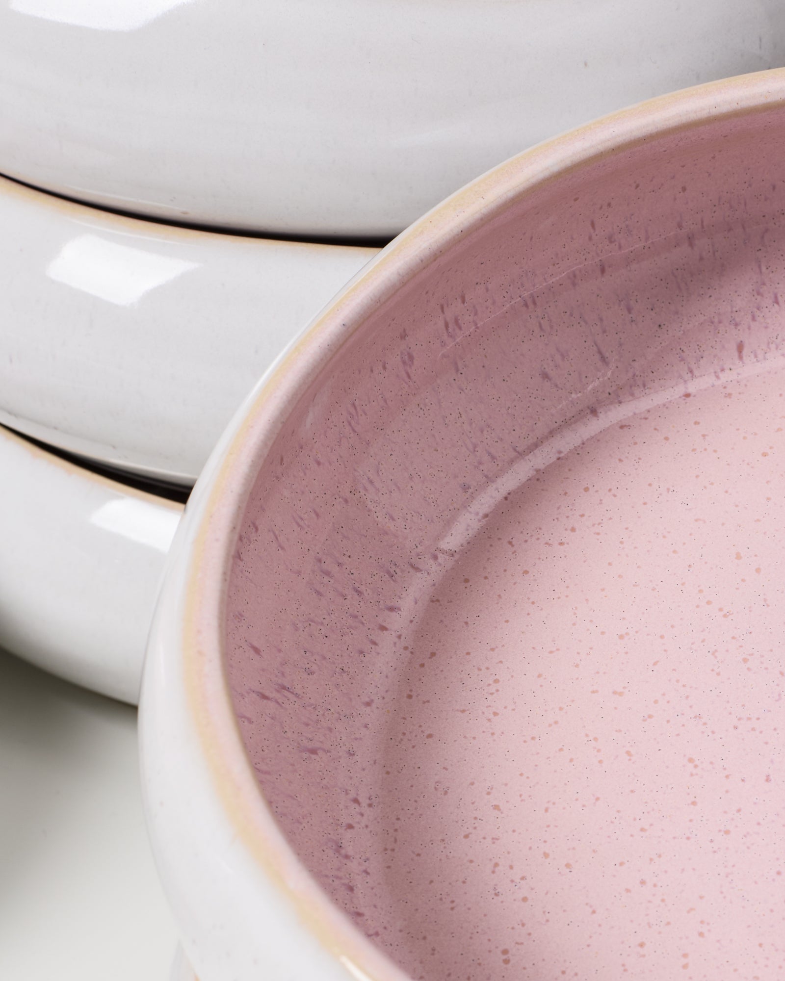 Nahaufnahme von gestapeltem Keramikgeschirr mit hellrosa Innenflächen und weißem Äußeren.