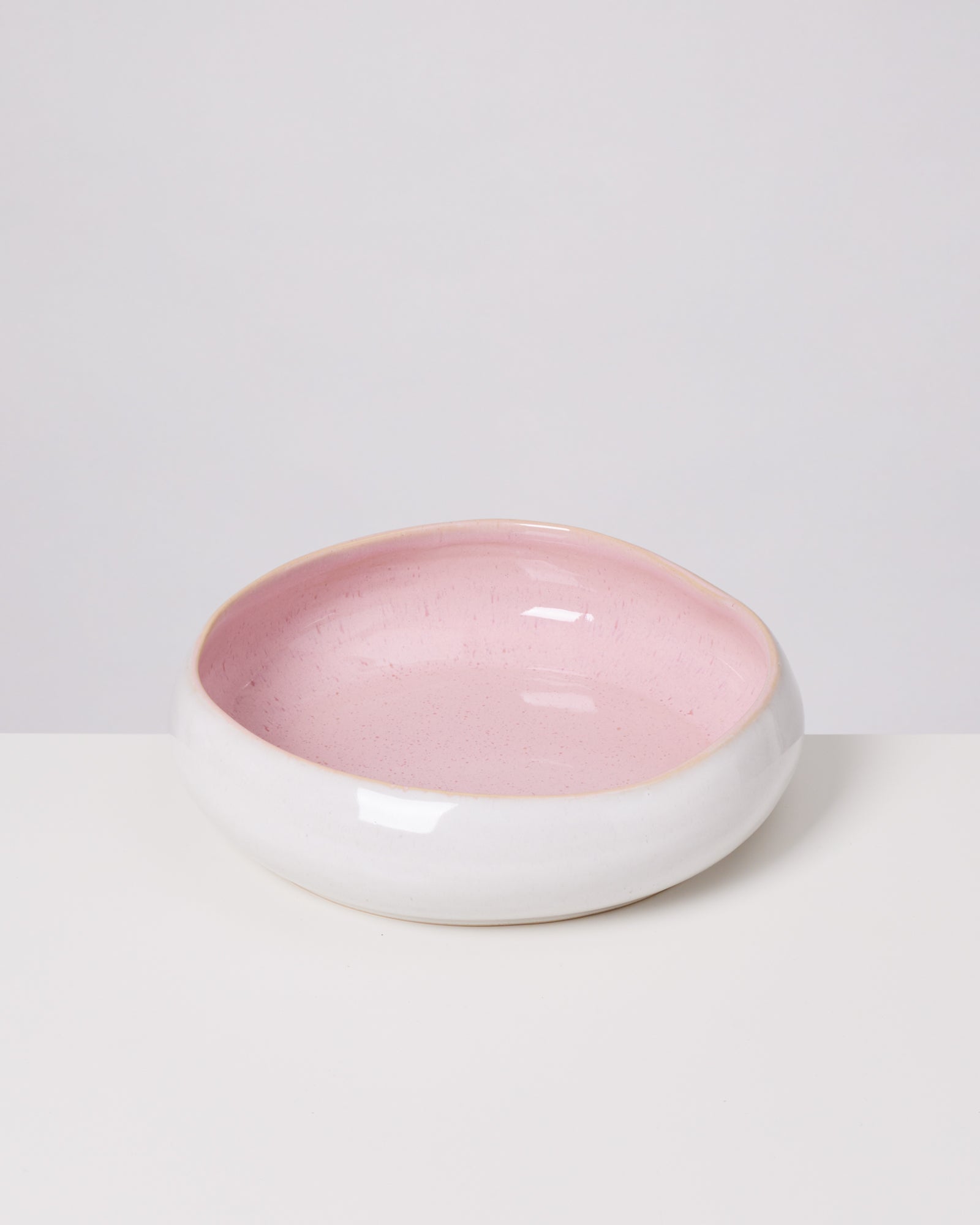 Eine runde Keramikschale mit rosa Innenseite und weißem Äußeren auf einem weißen Untergrund.