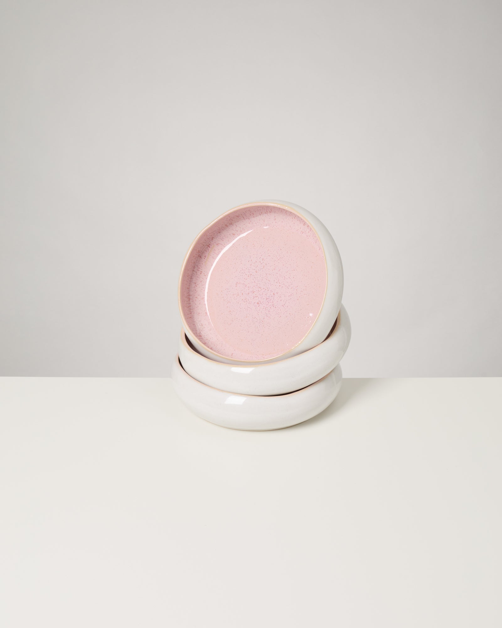 Drei gestapelte weiße Teller mit rosa Innenseite auf einem hellen Hintergrund.