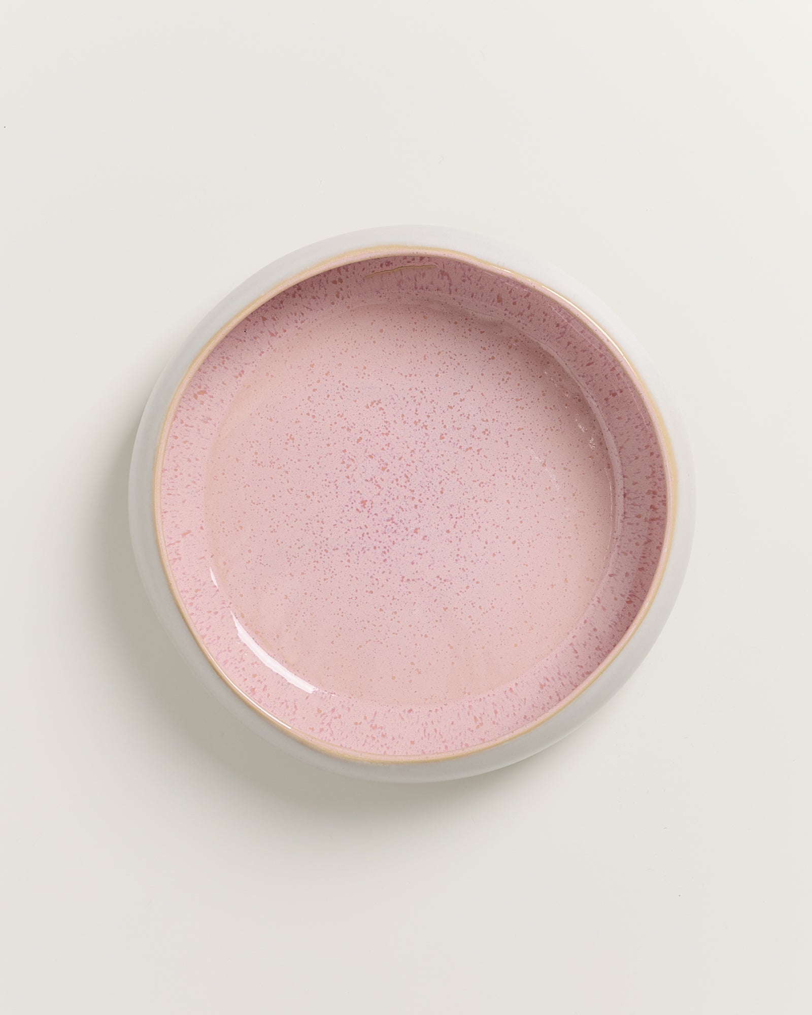 Runder, rosafarbener Keramikteller mit gesprenkelter Oberfläche auf einer weißen Hintergrundfläche.