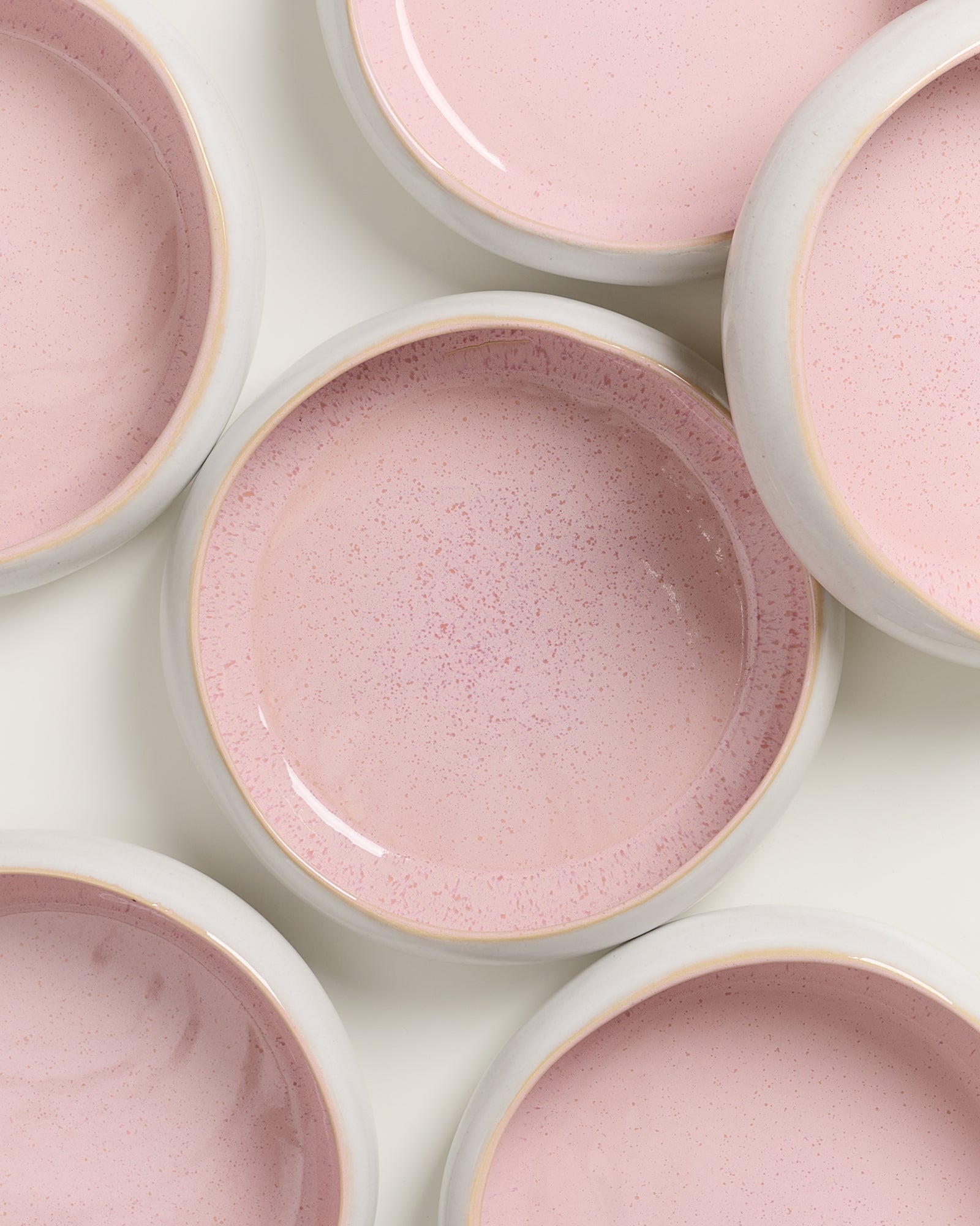Rosa Keramikschüsseln mit pastellfarbenen Innenseiten, aufgestellt auf einer weißen Oberfläche.