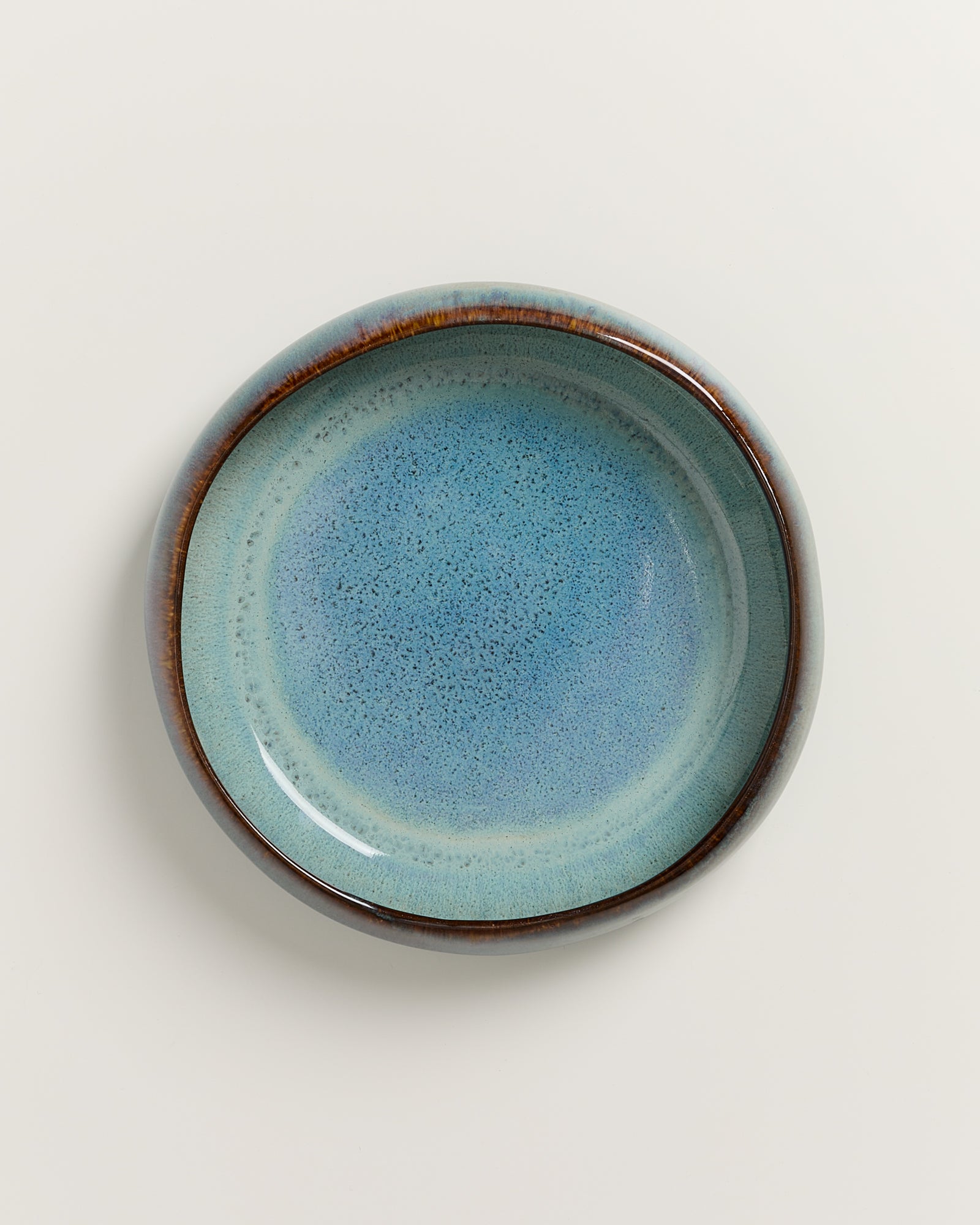 Runder Teller aus blauem Keramik mit glasiertem Finish auf weißem Hintergrund.