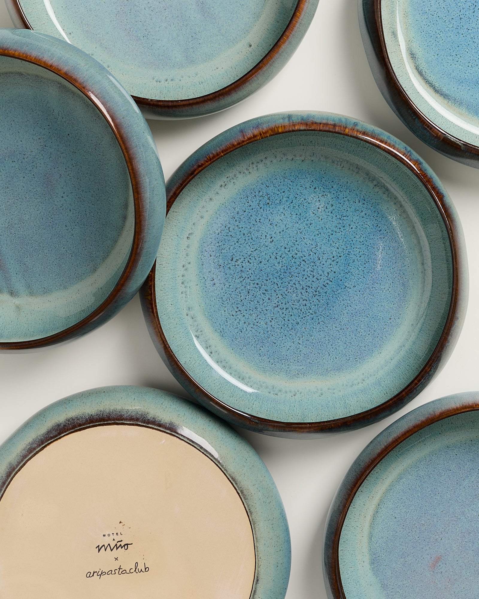 Mehrere blau glasierte Keramikteller, einer zeigt die Unterseite mit Markennamen.