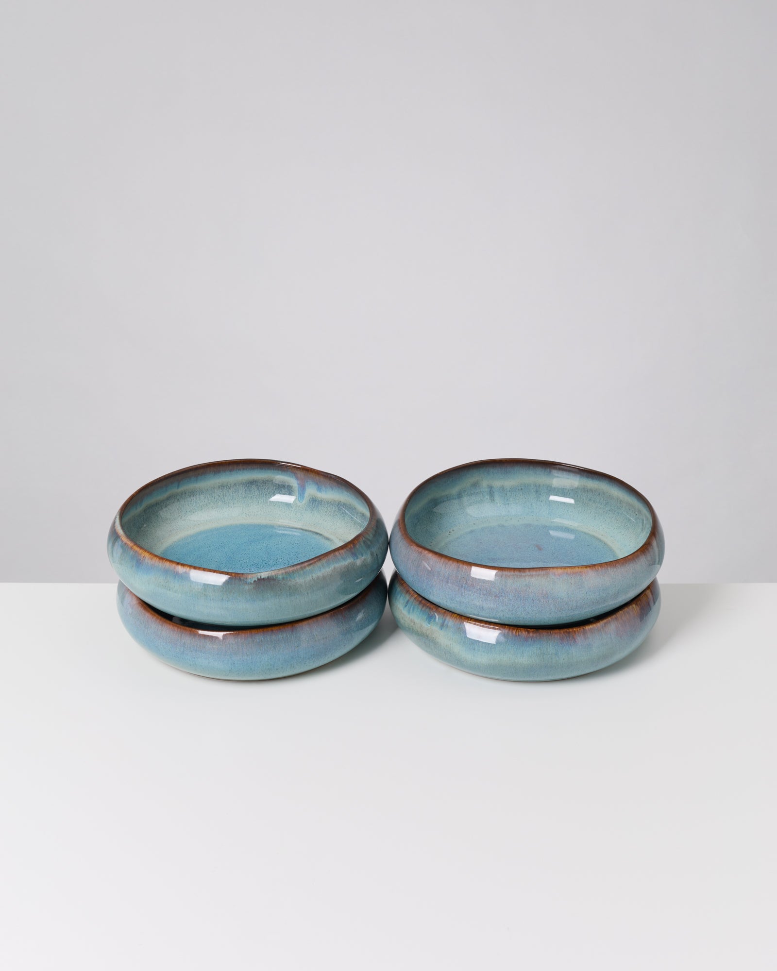 Vier gestapelte, blau glasierte Keramikschalen auf einem weißen Tisch vor grauem Hintergrund.