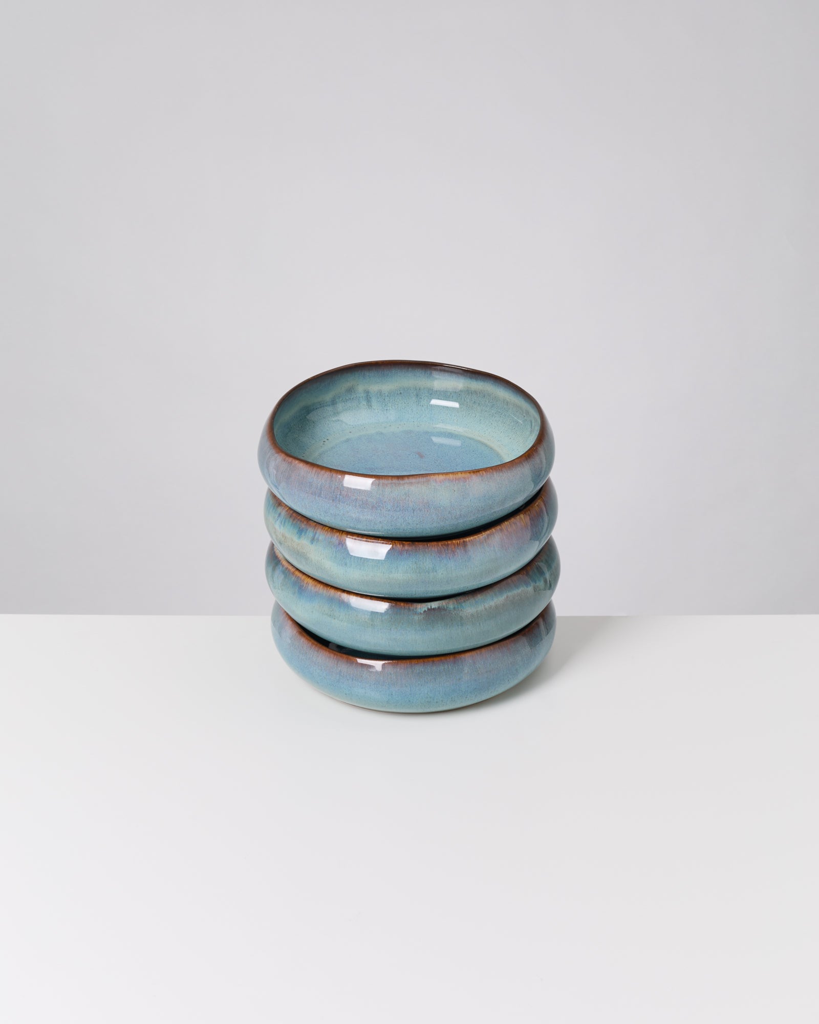 Vier türkisfarbene, glasierte Keramikschalen sind auf einem weißen Tisch gestapelt.