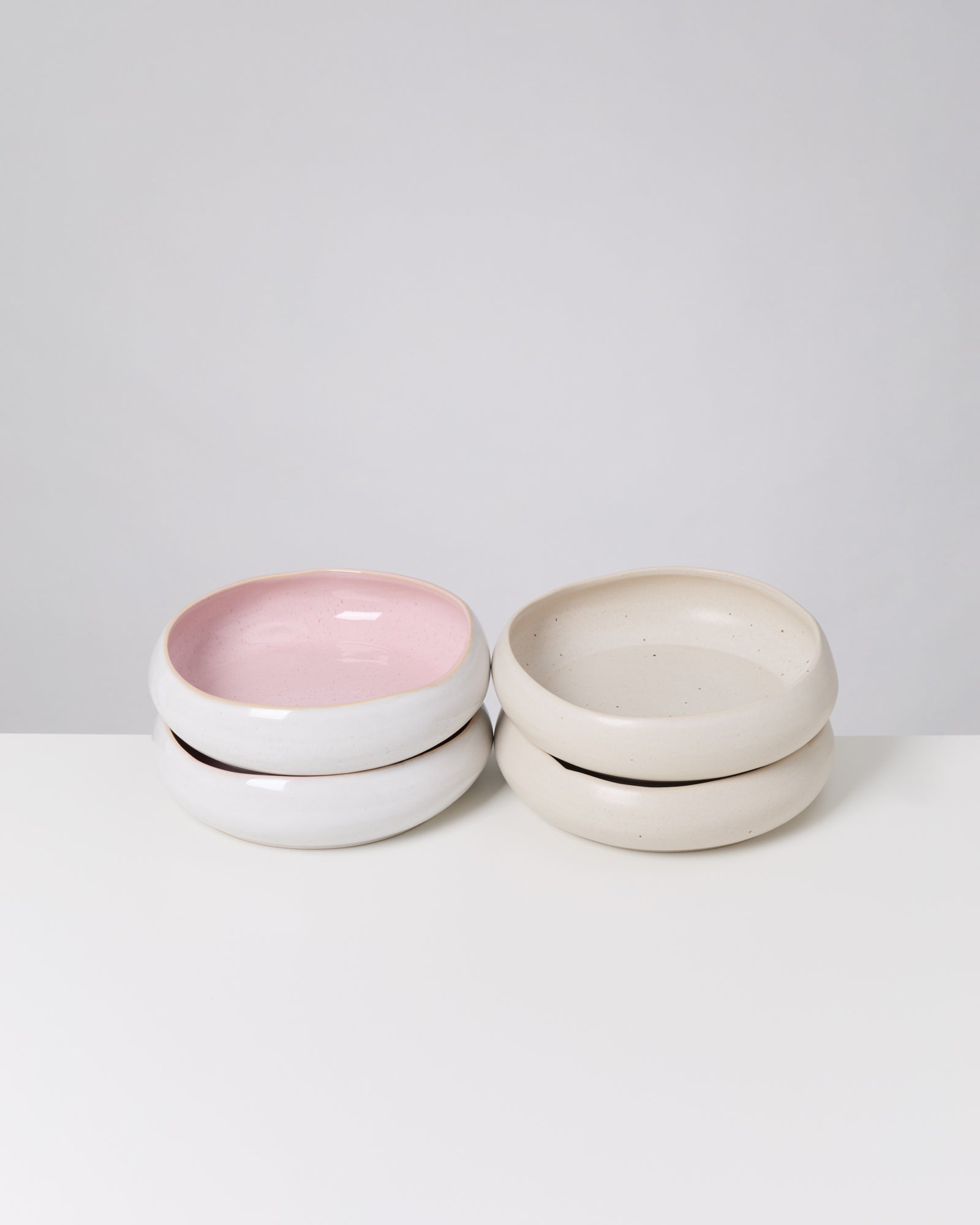 Vier gestapelte, flache Keramikschalen, zwei mit rosa Innenfläche, auf einem weißen Hintergrund.