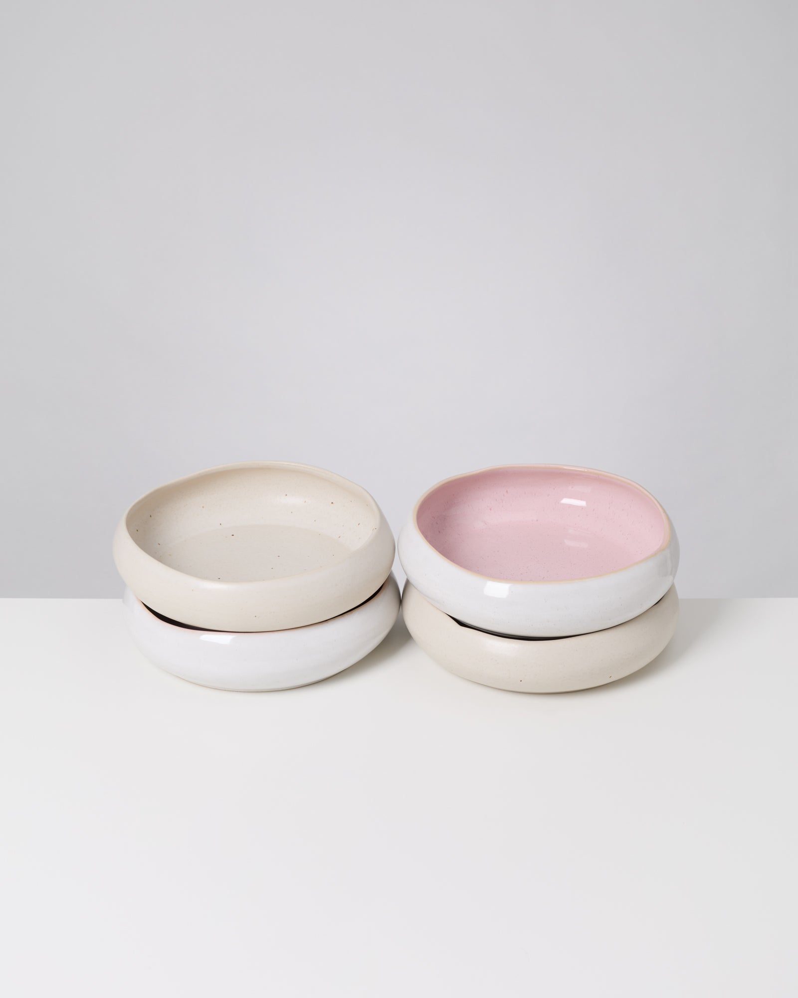 Vier gestapelte Schalen mit zwei weißen und zwei rosa Innenflächen auf einem weißen Hintergrund.