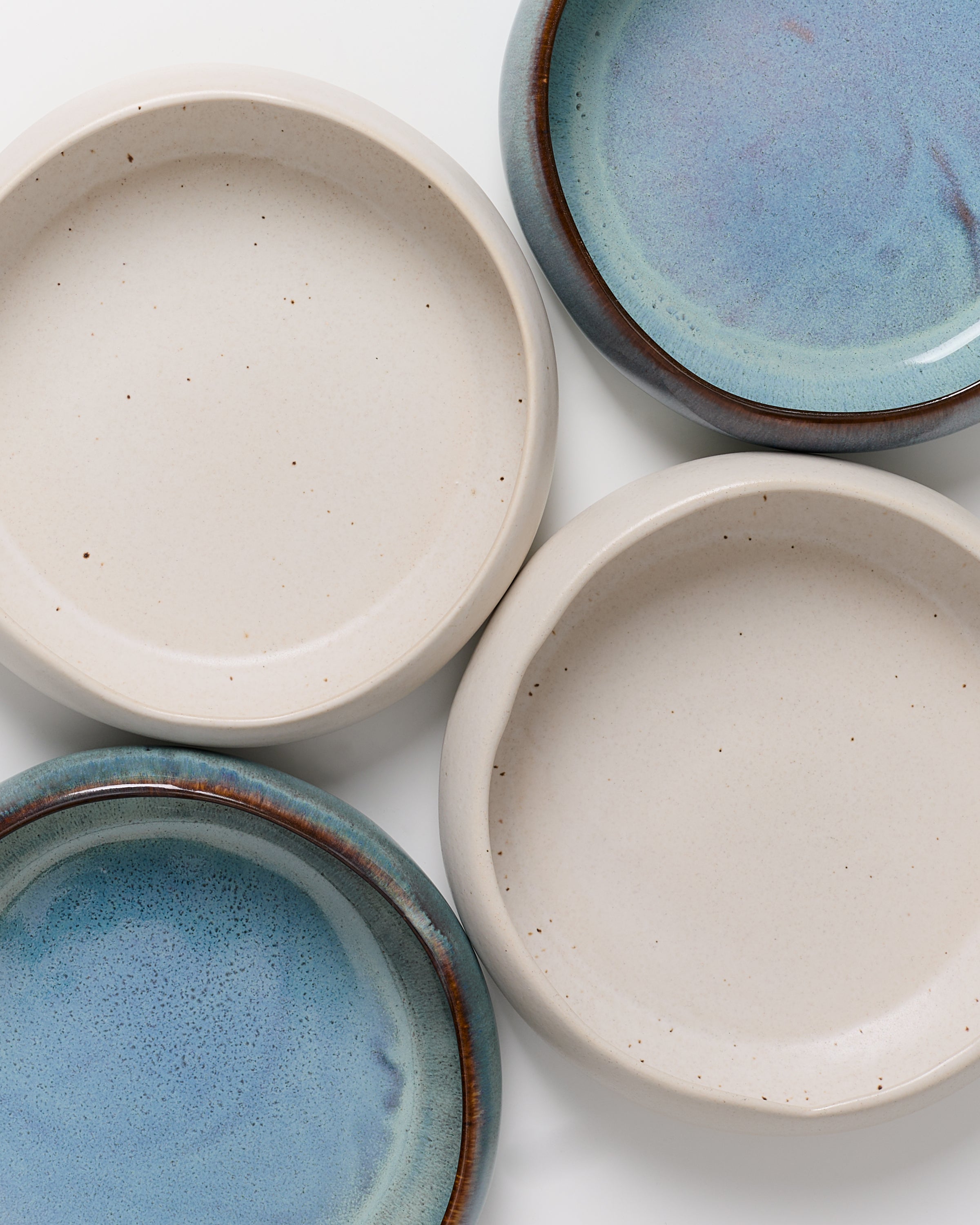 Vier Keramikteller, zwei in cremefarben und zwei in blau, liegen auf einer weißen Oberfläche.