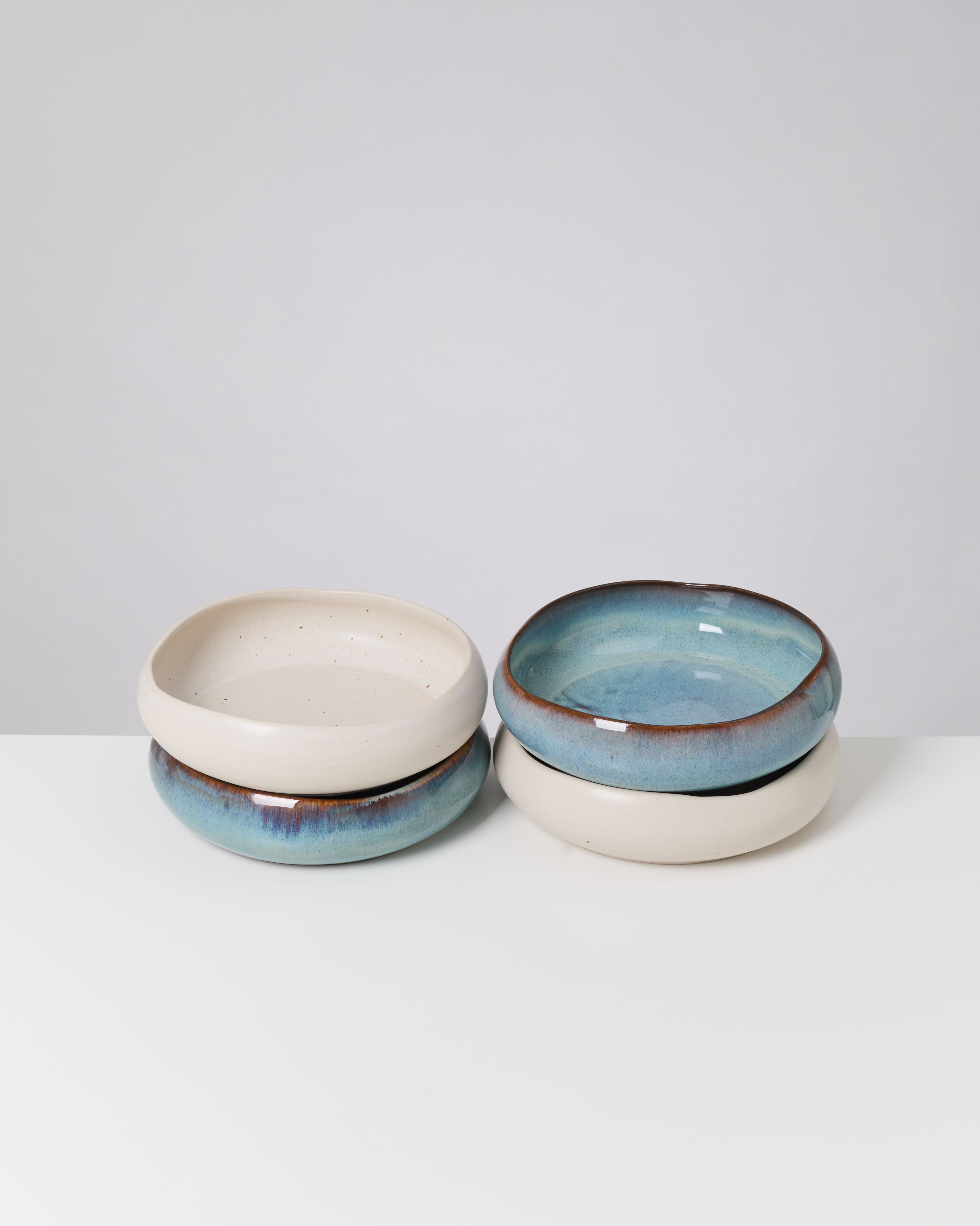 Zwei gestapelte Keramikschalen, eine mit blauer Glasur, auf einem weißen Hintergrund.