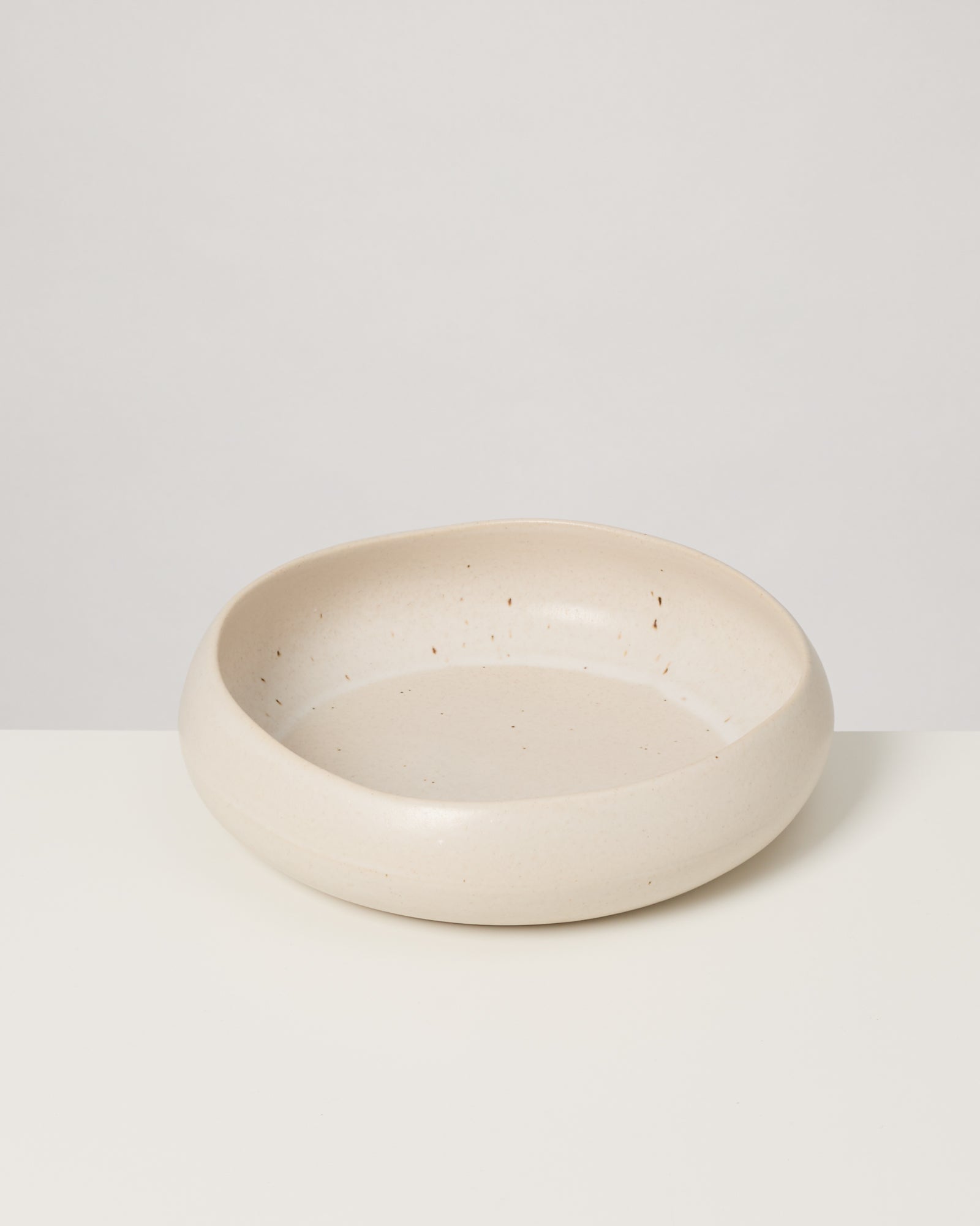 Beiger, flacher Keramikteller mit leicht unregelmäßiger Form auf einem weißen Hintergrund.