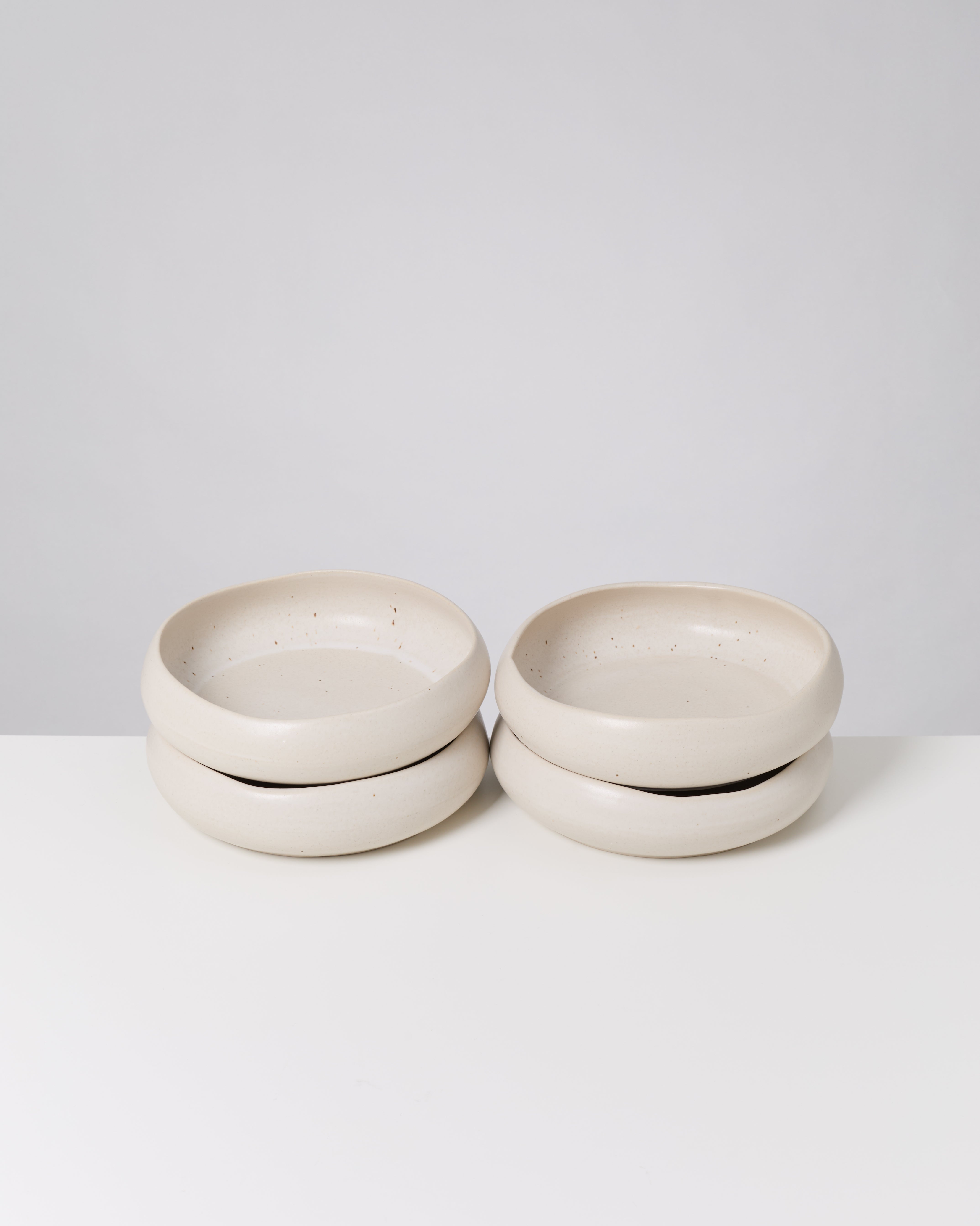 Vier stapelbare, beige Keramikschalen auf einer weißen Oberfläche vor einem grauen Hintergrund.