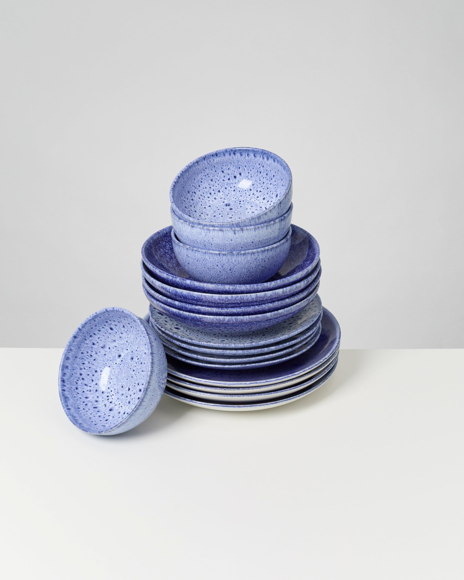 Ein Stapel aus blauen Tellern und Schalen auf einem weißen Tisch, eine Schale liegt daneben.