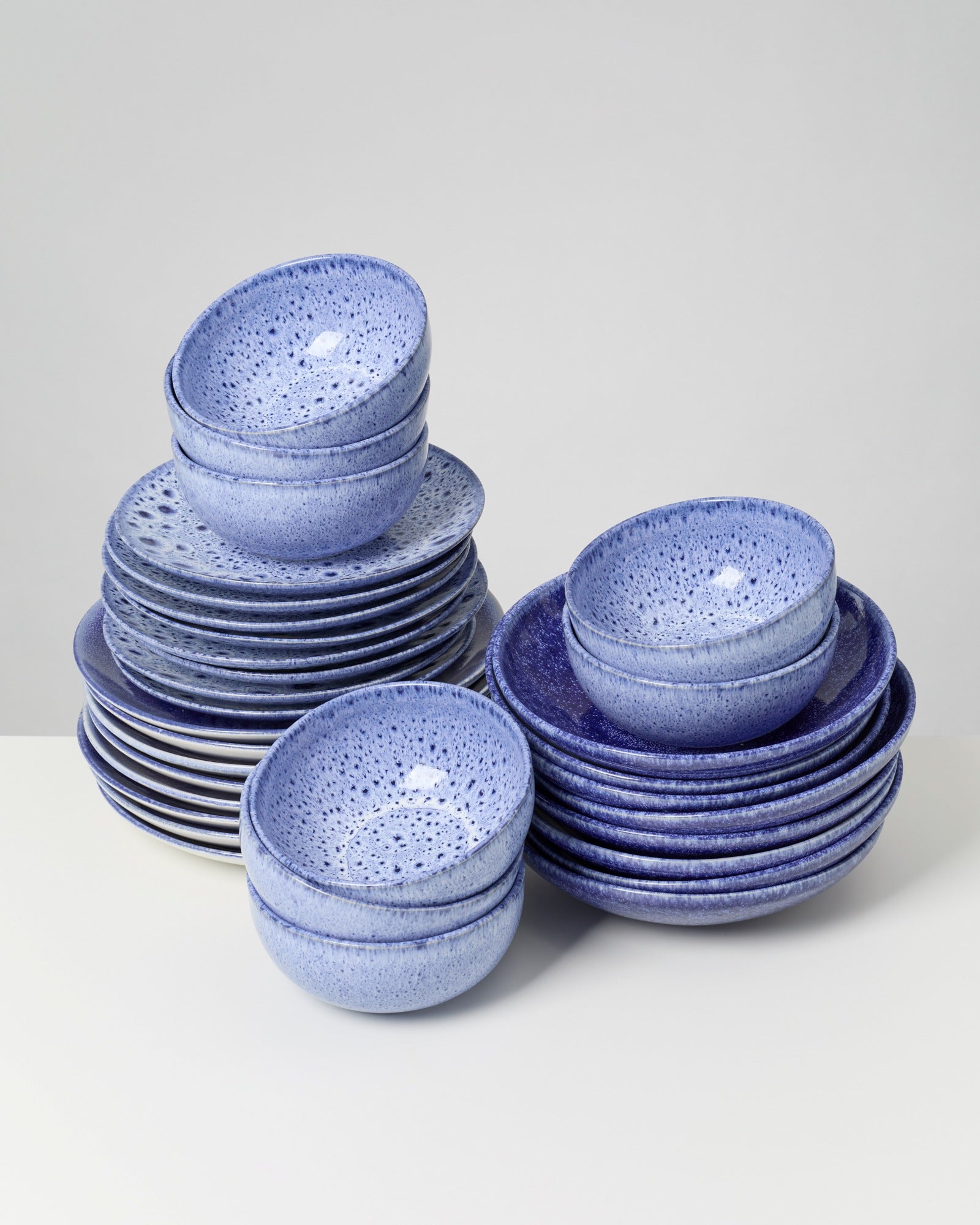 Zwei Stapel aus blauen, gesprenkelten Keramikschalen und Tellern auf einer weißen Oberfläche.