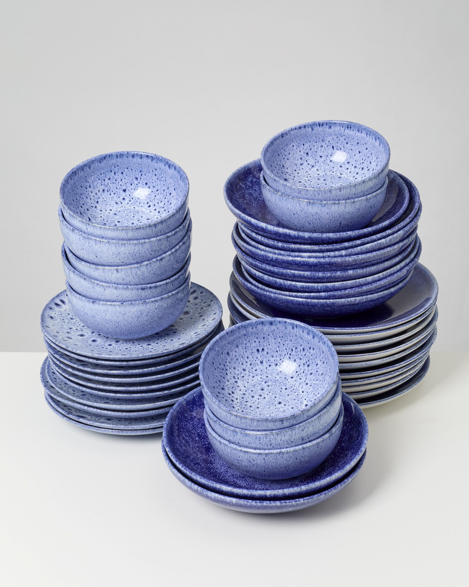 Gestapelte, blaue Keramikschalen und -teller mit gesprenkeltem Muster auf einem Tisch.