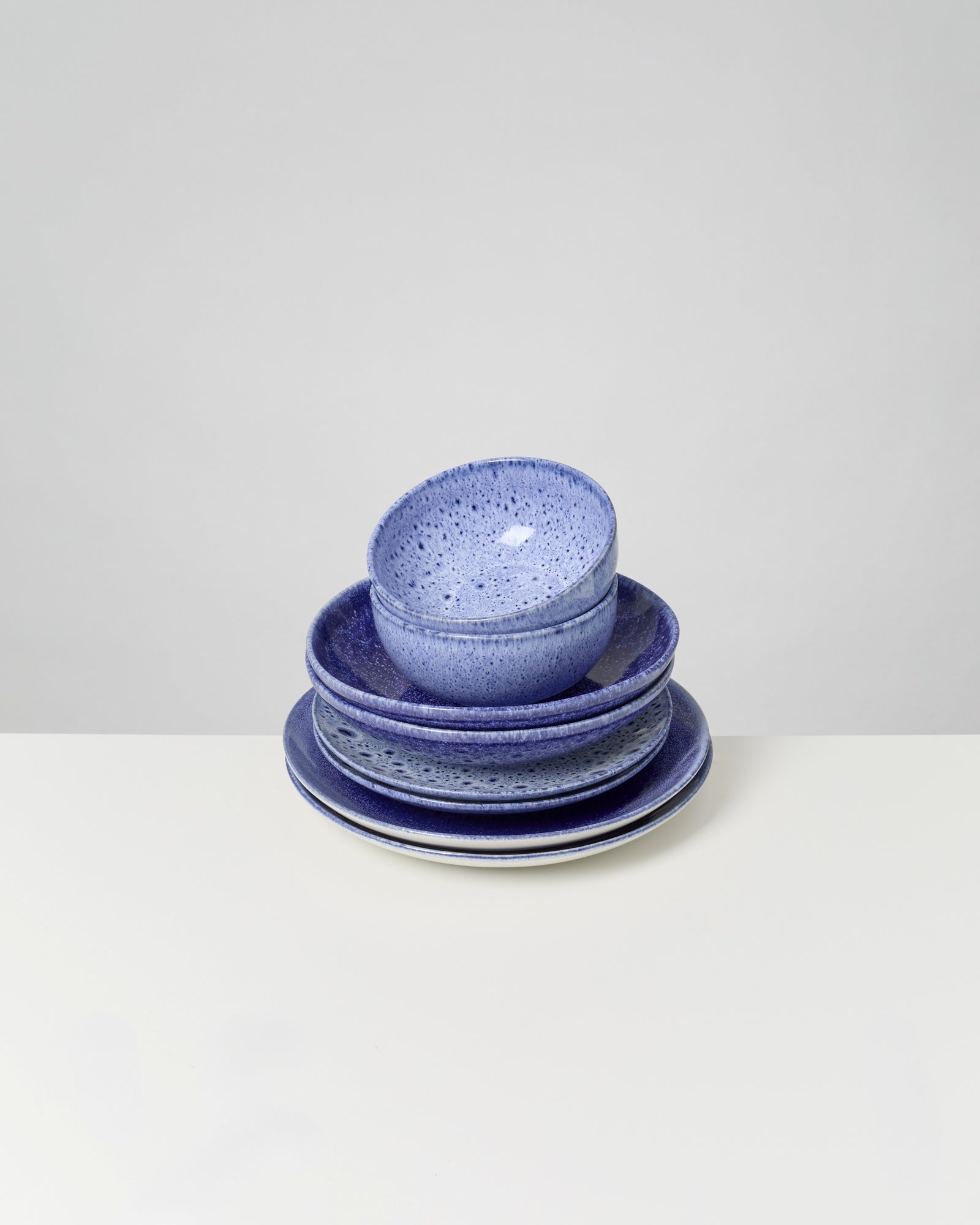 Ein Stapel aus blauen, gesprenkelten Keramiktellern und -schalen auf einem weißen Hintergrund.
