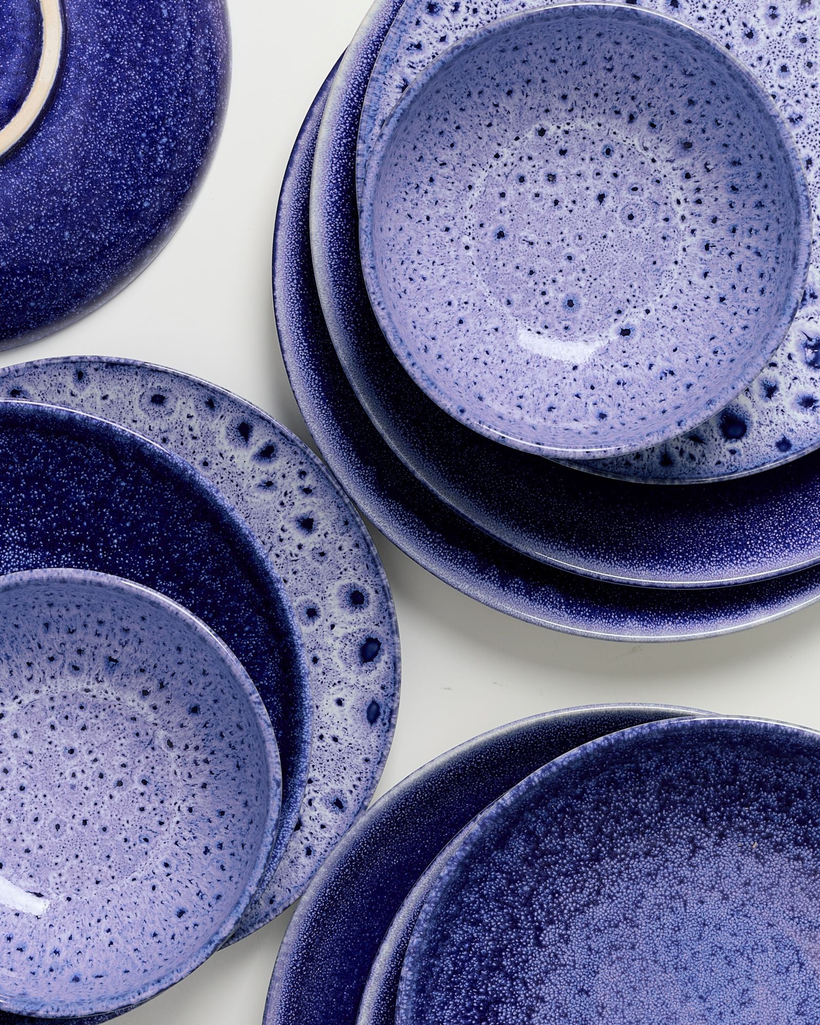 Verschiedene gestapelte Teller und Schalen in Blau- und Lilatönen mit gesprenkeltem Muster auf weißem Hintergrund.
