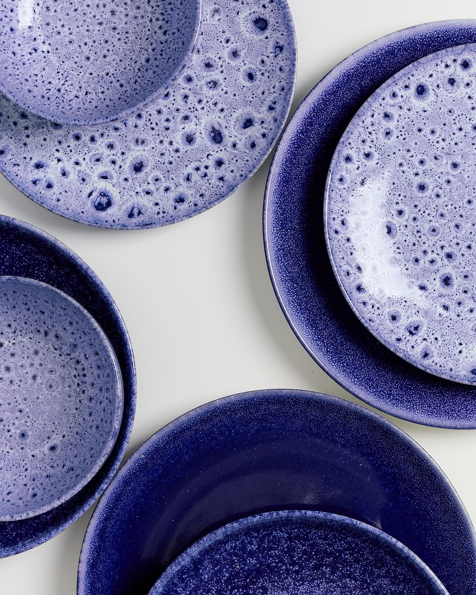 Verschiedene lila Keramikteller mit gesprenkeltem Muster liegen auf einer weißen Oberfläche.