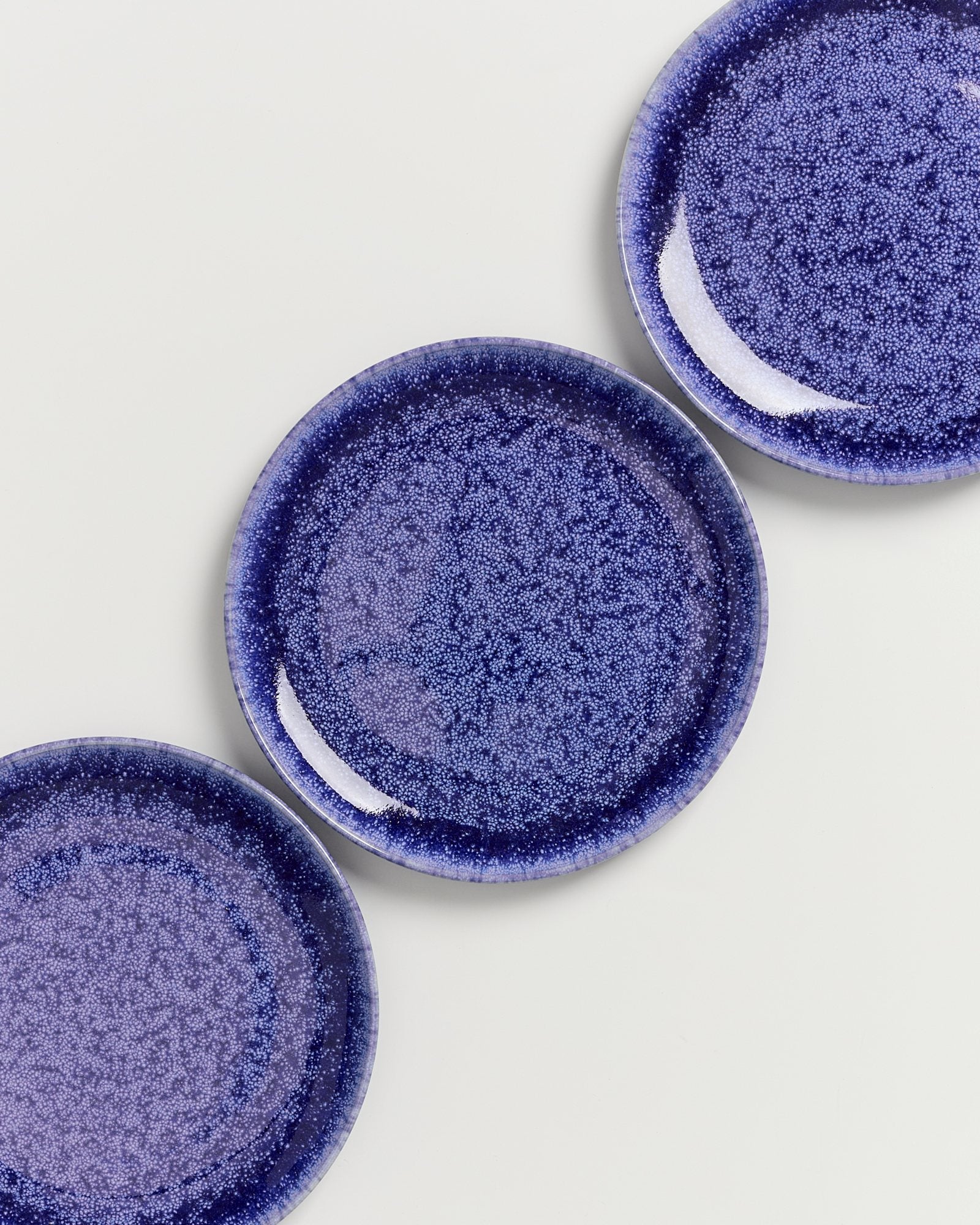 Drei blaue, gesprenkelte Teller auf weißem Hintergrund, teilweise überlappend angeordnet.