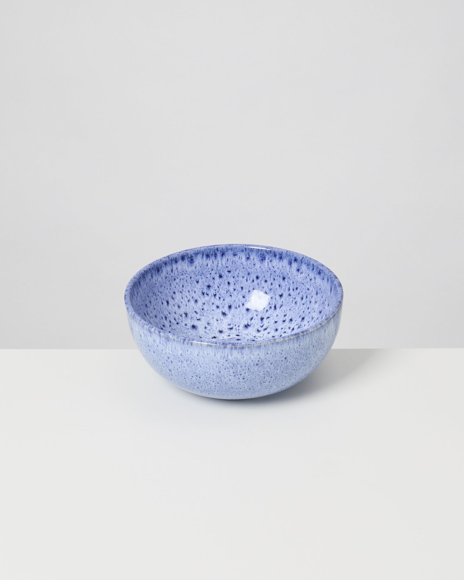 Eine blaue, gesprenkelte Keramikschale steht auf einem weißen Tisch vor grauem Hintergrund.
