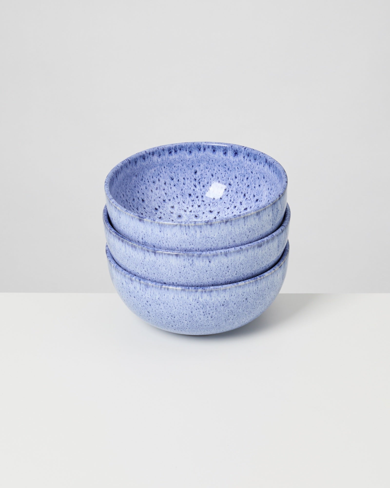 Drei gestapelte blaue Keramikschüsseln mit gesprenkeltem Muster stehen auf einem weißen Tisch.