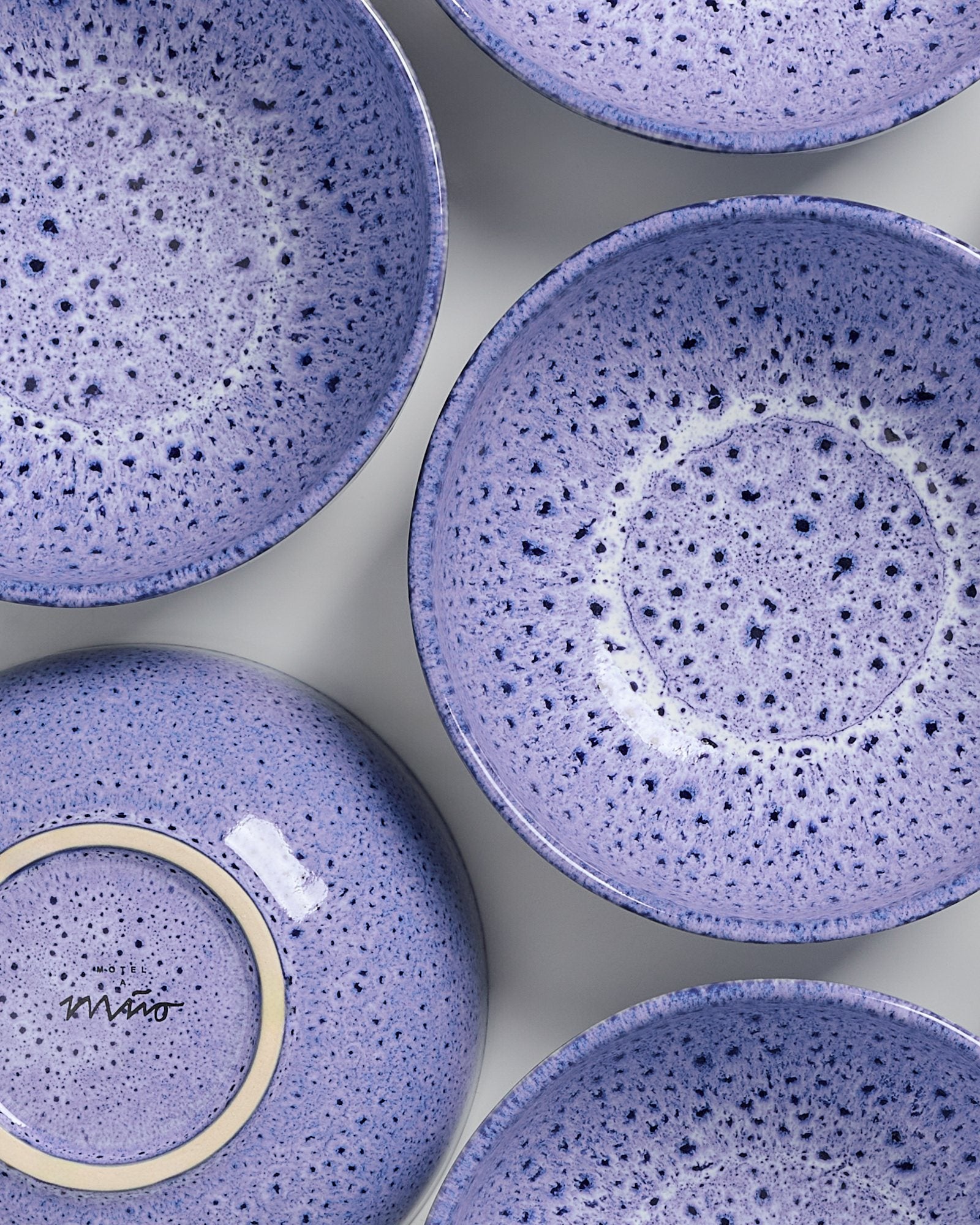 Fünf lilafarbene Keramikteller mit gesprenkeltem Muster auf grauem Hintergrund.
