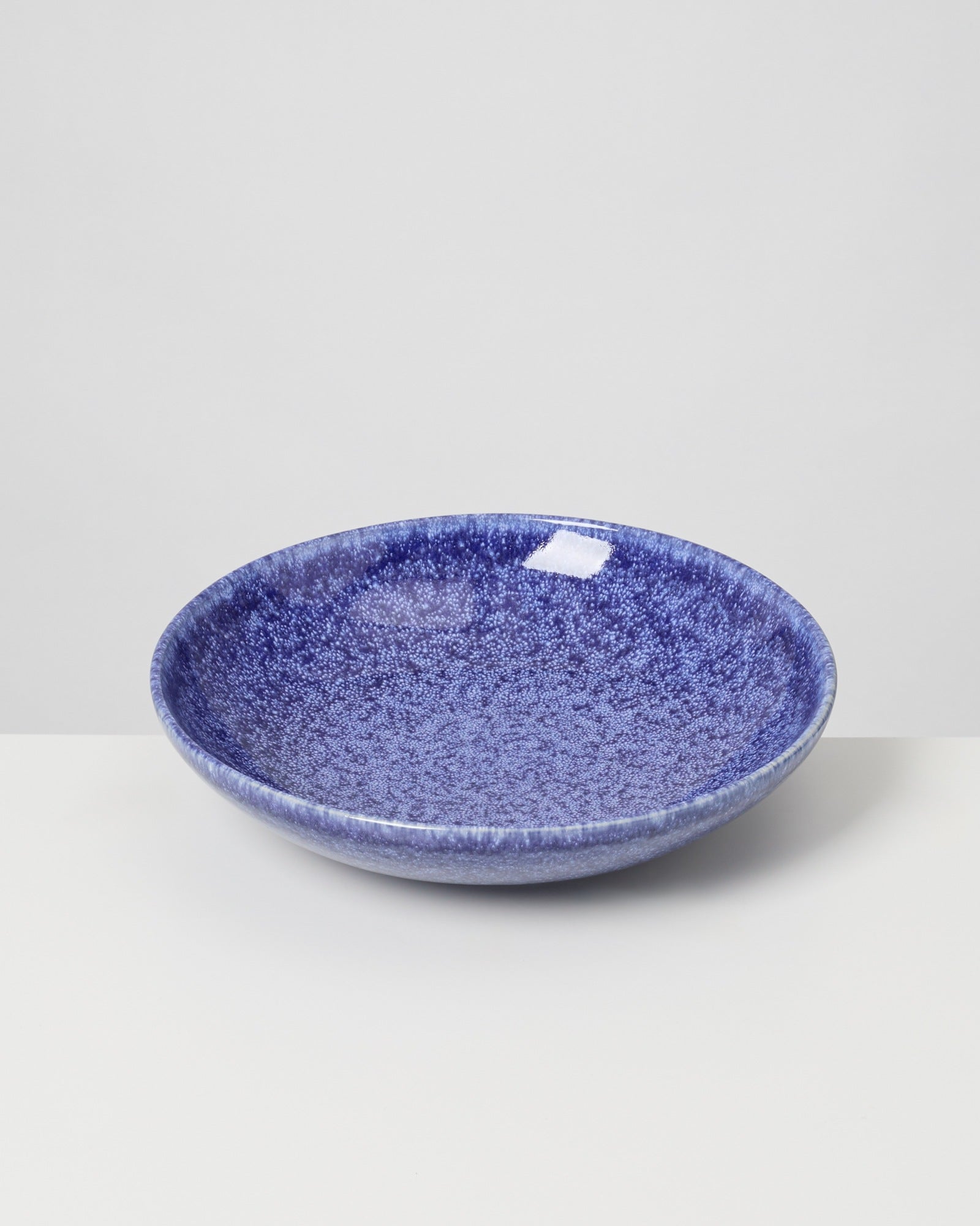 Blaue, runde Keramikschale mit gesprenkeltem Muster auf hellem Hintergrund.