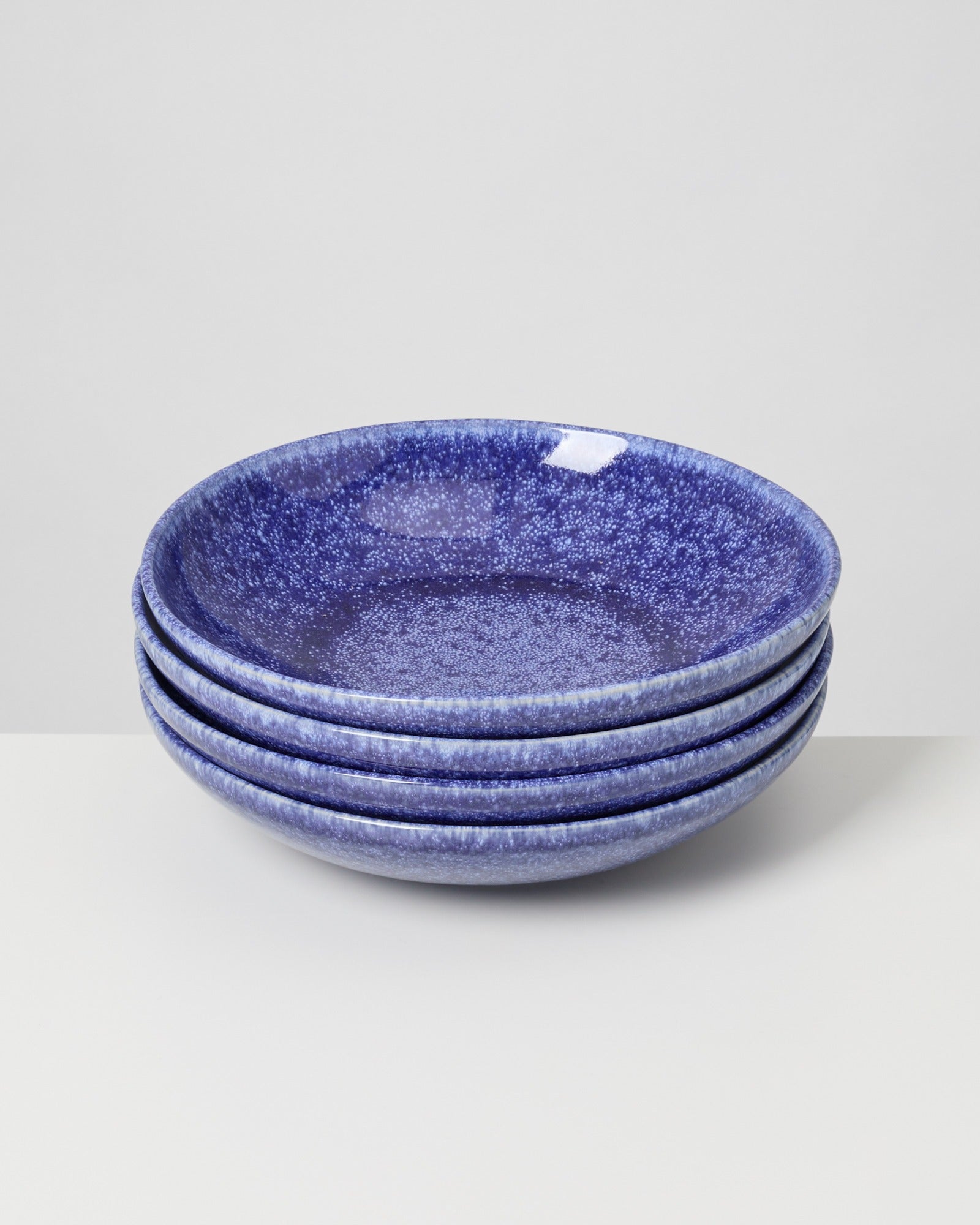 Ein Stapel aus fünf blauen, gesprenkelten Tellern auf einem weißen Hintergrund.