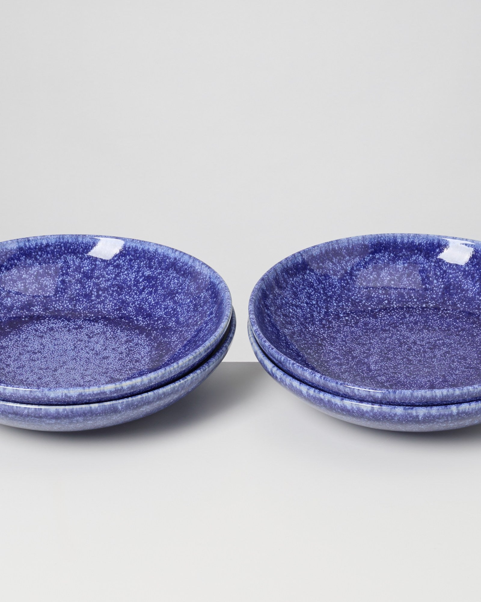 Vier blaue, gesprenkelte Teller in zwei Stapeln auf einem weißen Hintergrund.