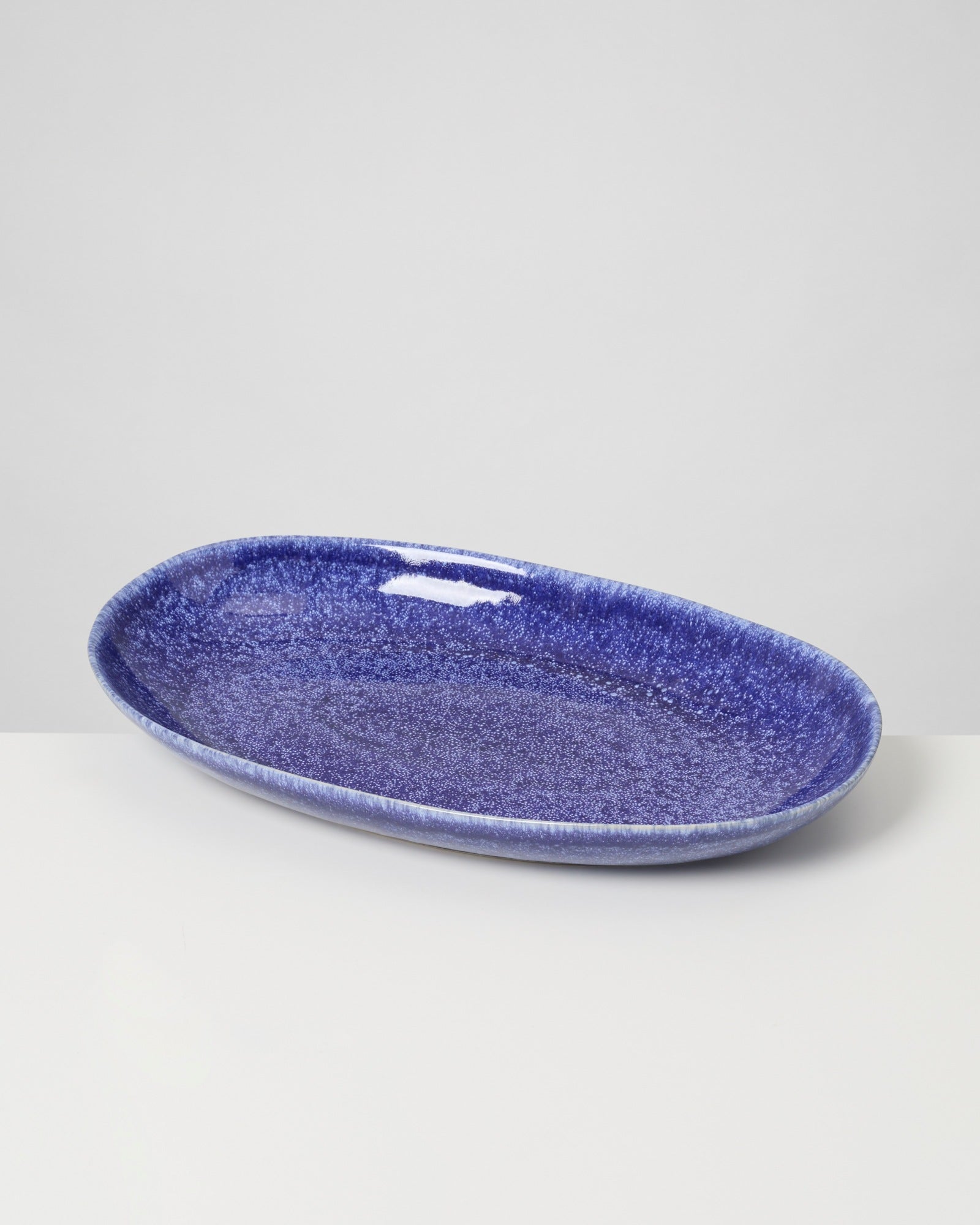 Ovaler blauer Keramikteller mit glänzender Oberfläche auf weißem Hintergrund.