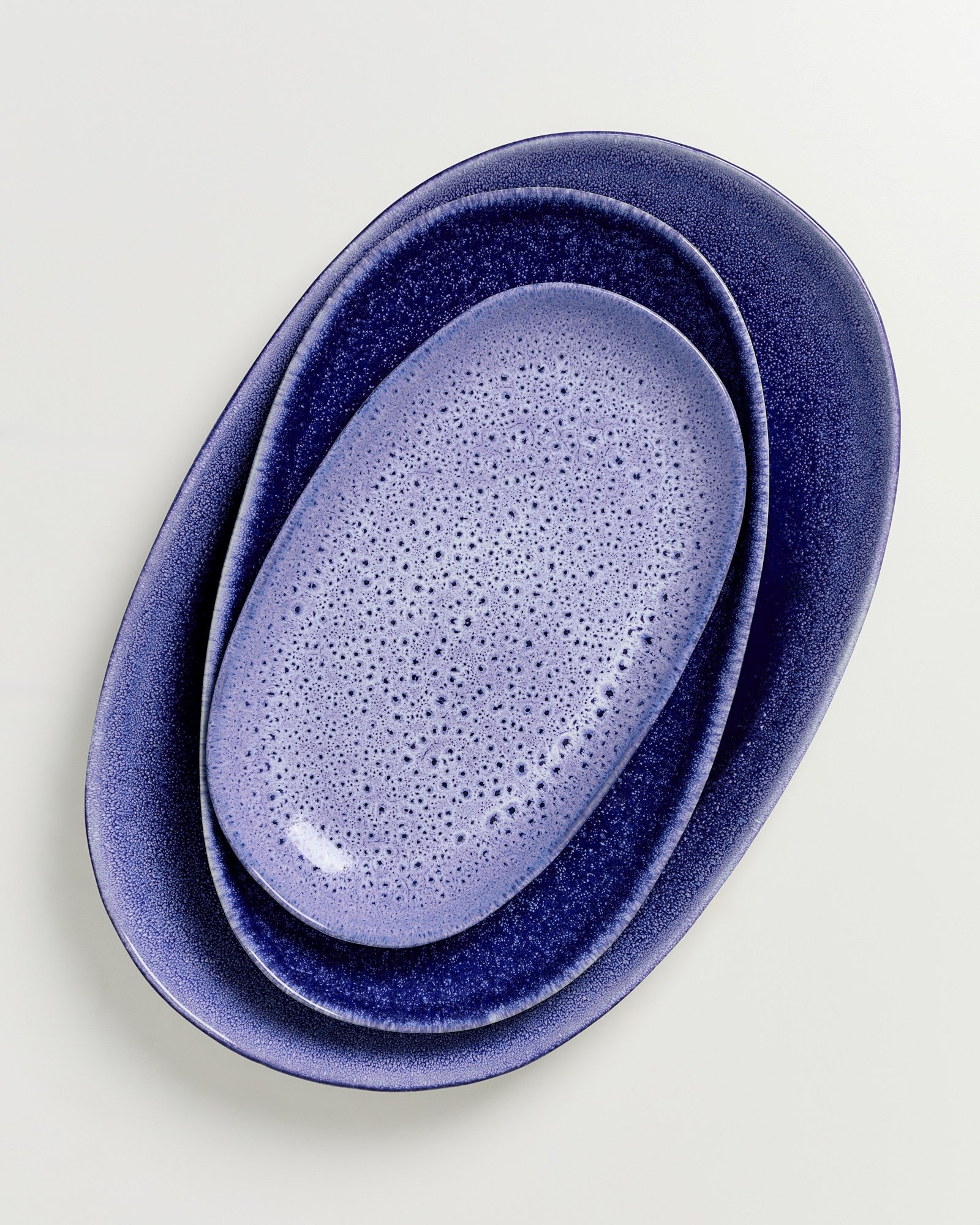 Drei ineinanderliegende ovale Teller in verschiedenen Blautönen auf einem hellen Hintergrund.