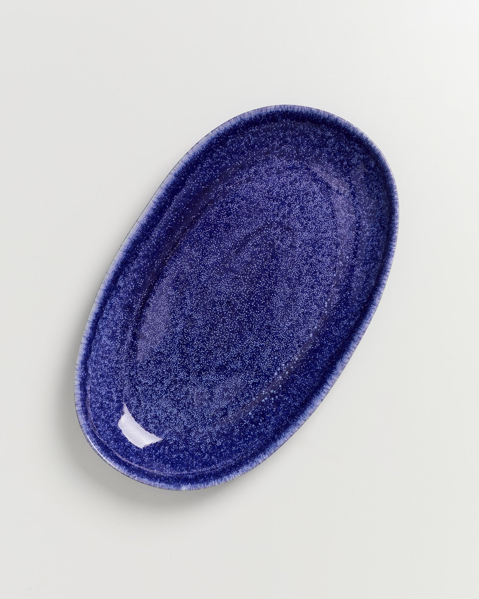 Blauer ovaler Teller mit gesprenkelter Oberfläche auf hellem Hintergrund.