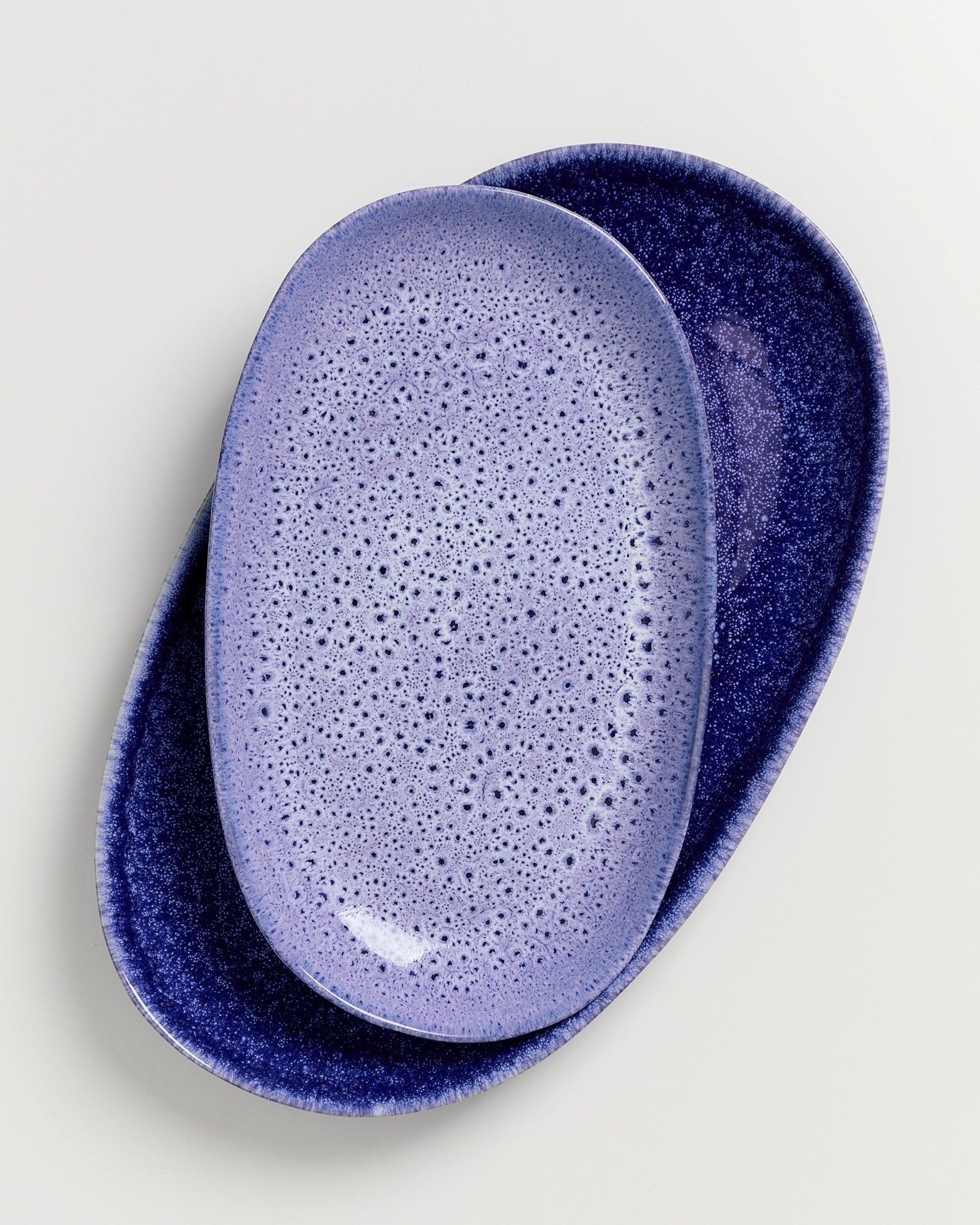 Zwei ovale Teller in Blau- und Lilatönen mit gesprenkelter Oberfläche übereinander gestapelt.