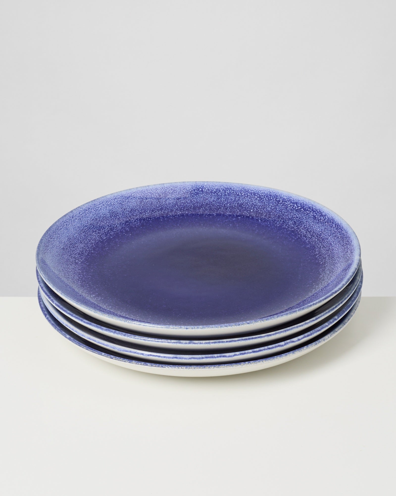 Ein Stapel von vier blauen Tellern mit hellen Rändern auf einem hellen Untergrund.