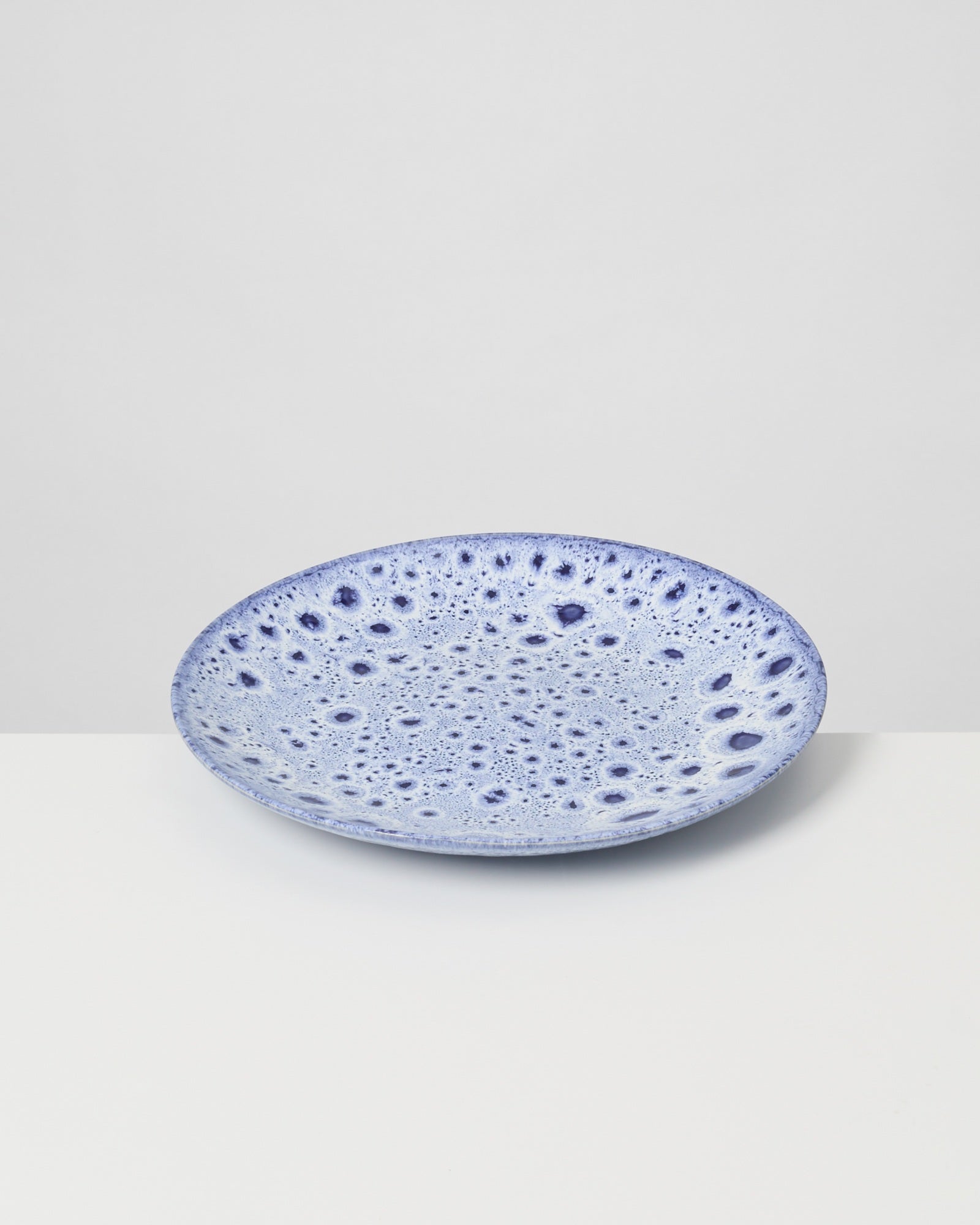 Blauer Teller mit auffälligem, tropfenähnlichem Muster auf weißem Hintergrund.