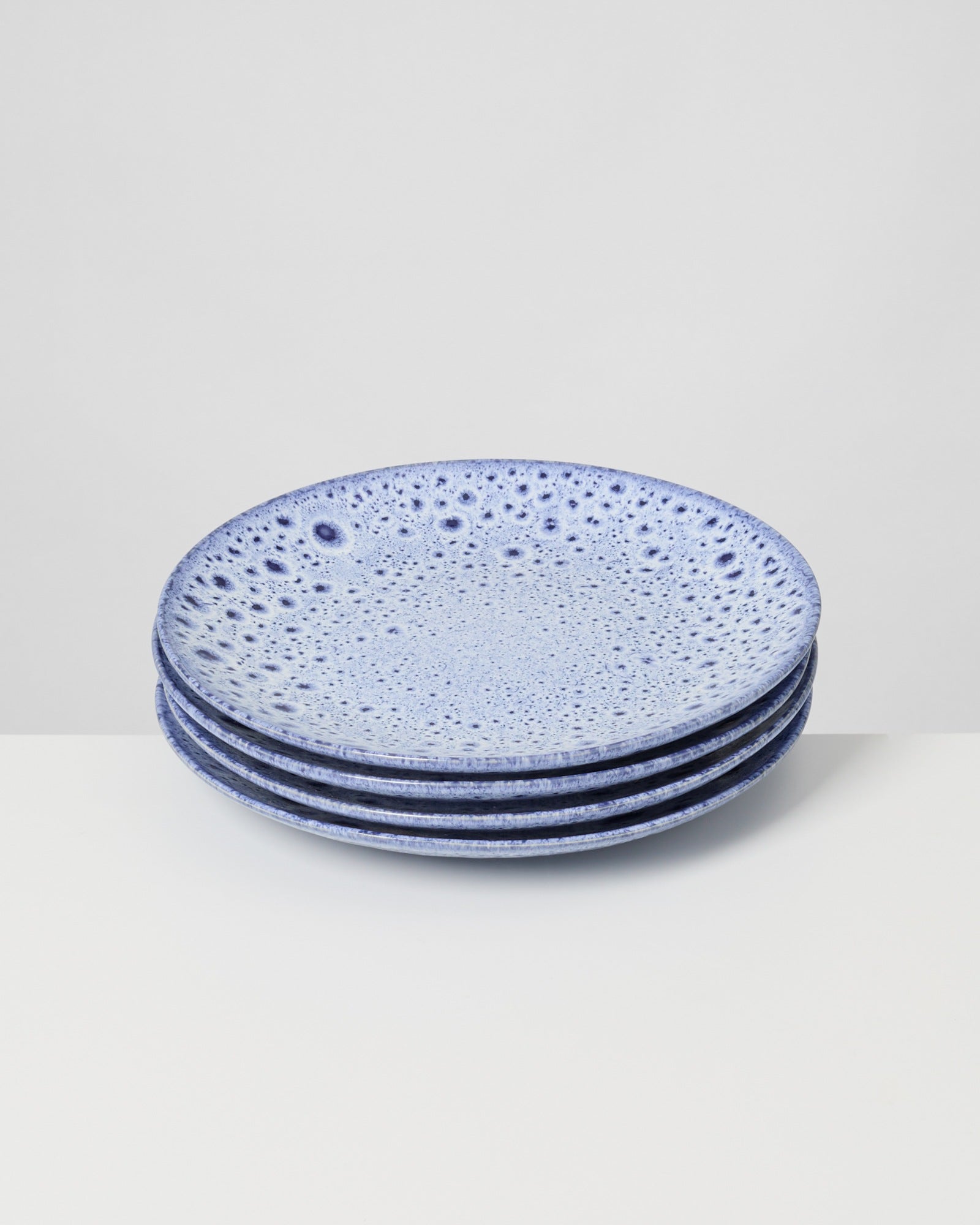 Vier blaue, gemusterte Teller sind aufeinander gestapelt und auf einem weißen Tisch platziert.