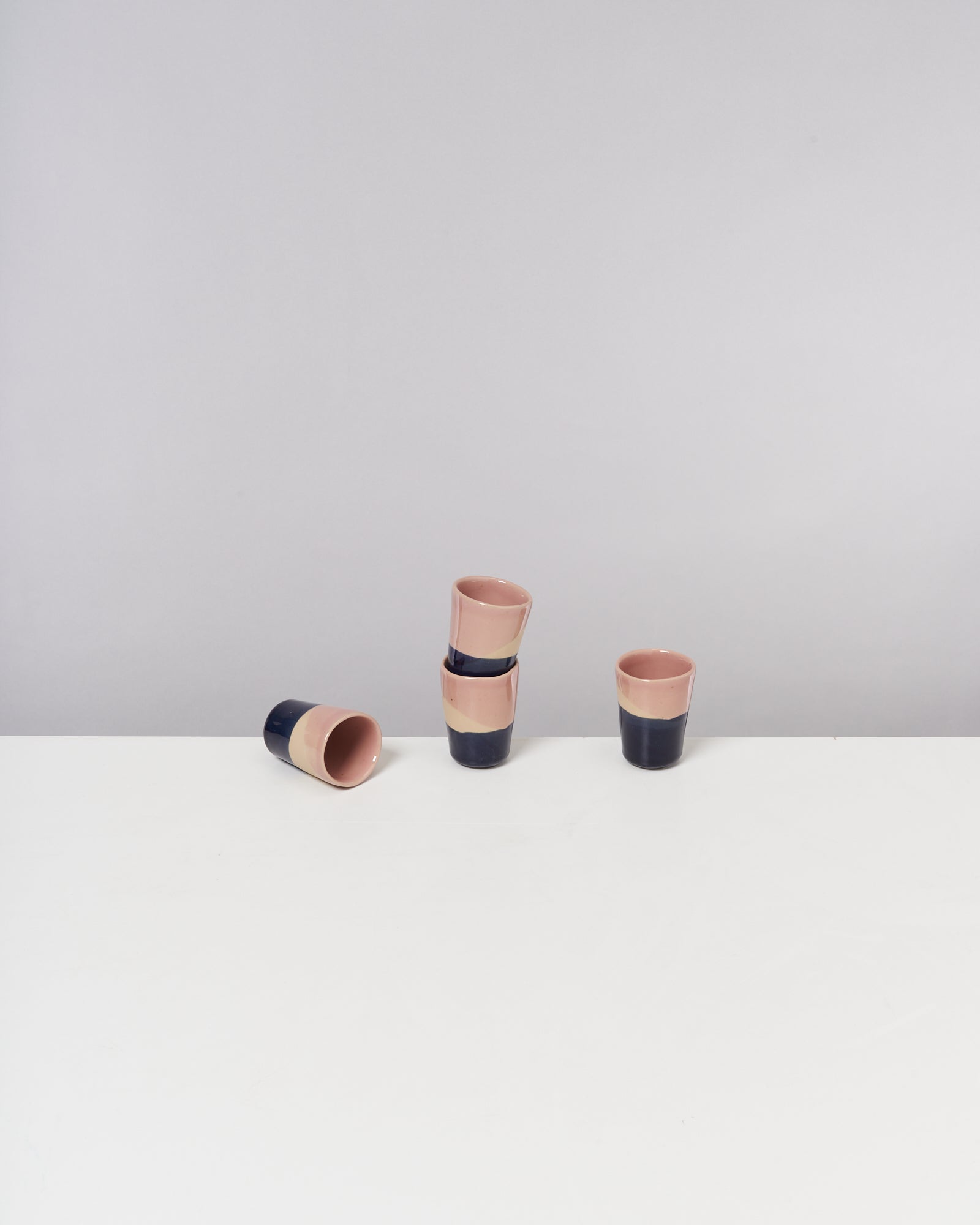 Vier rosa und dunkelblaue Becher auf einem weißen Tisch, zwei gestapelt, einer stehend, einer liegend.