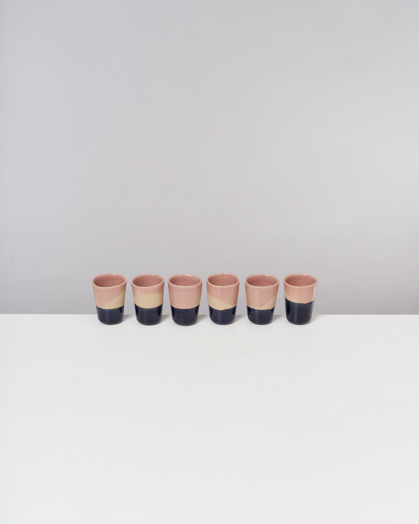 Sechs pastellfarbene Keramiktassen mit diagonalen Streifen stehen in einer Reihe auf einem weißen Tisch.