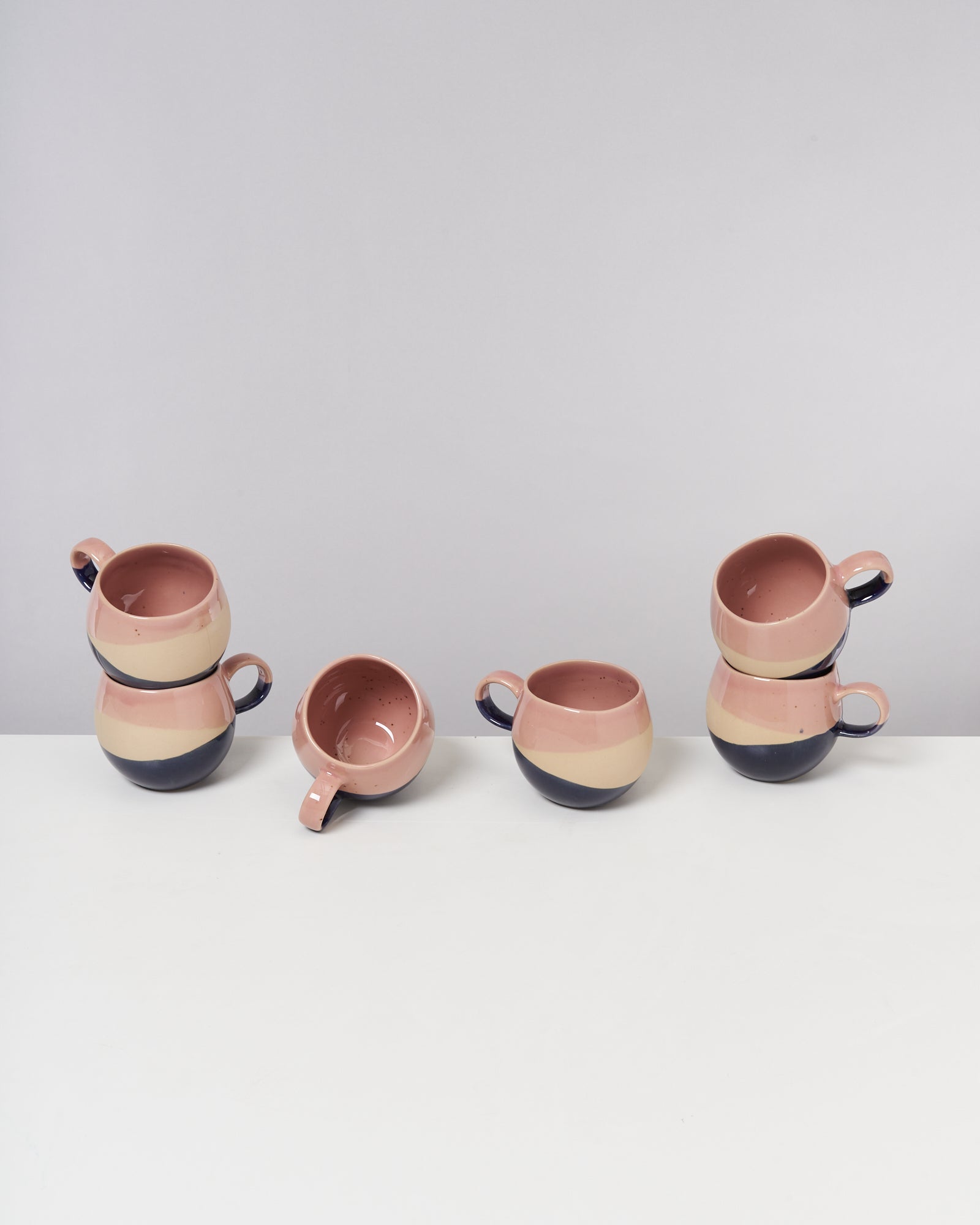 Drei Stapel aus je zwei rosa-beigen Tassen auf weißem Tisch; eine vierte Tasse liegt seitlich daneben.