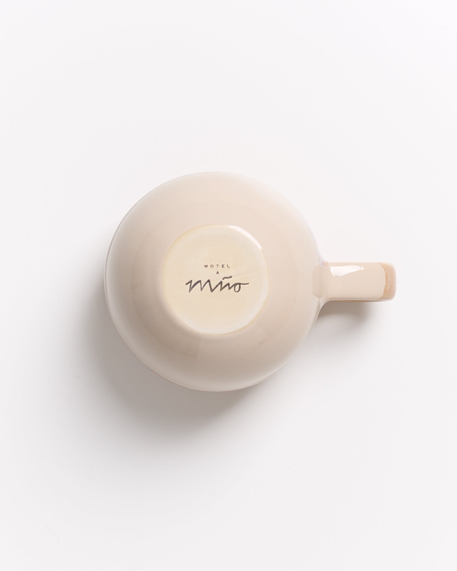 Beigefarbene Tasse von unten mit Schriftzug "Hotel A Mino" auf hellem Hintergrund.