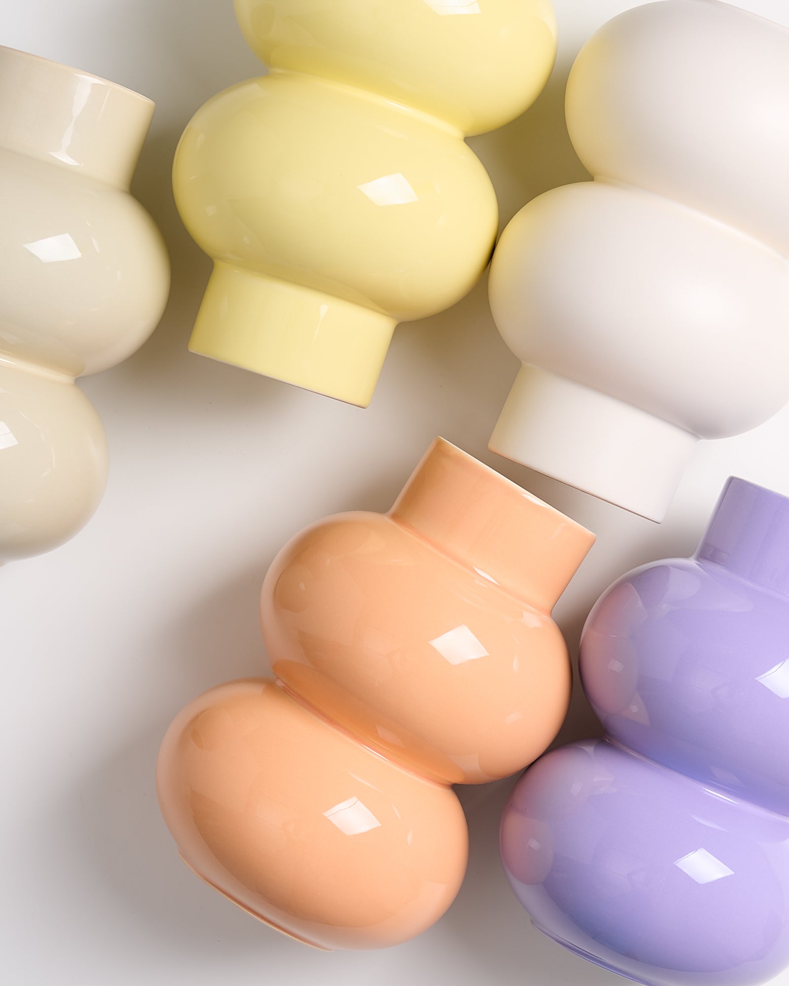 Fünf bunte, kugelförmige Vasen in Pastelltönen (beige, gelb, weiß, orange, lila) auf einem weißen Hintergrund.