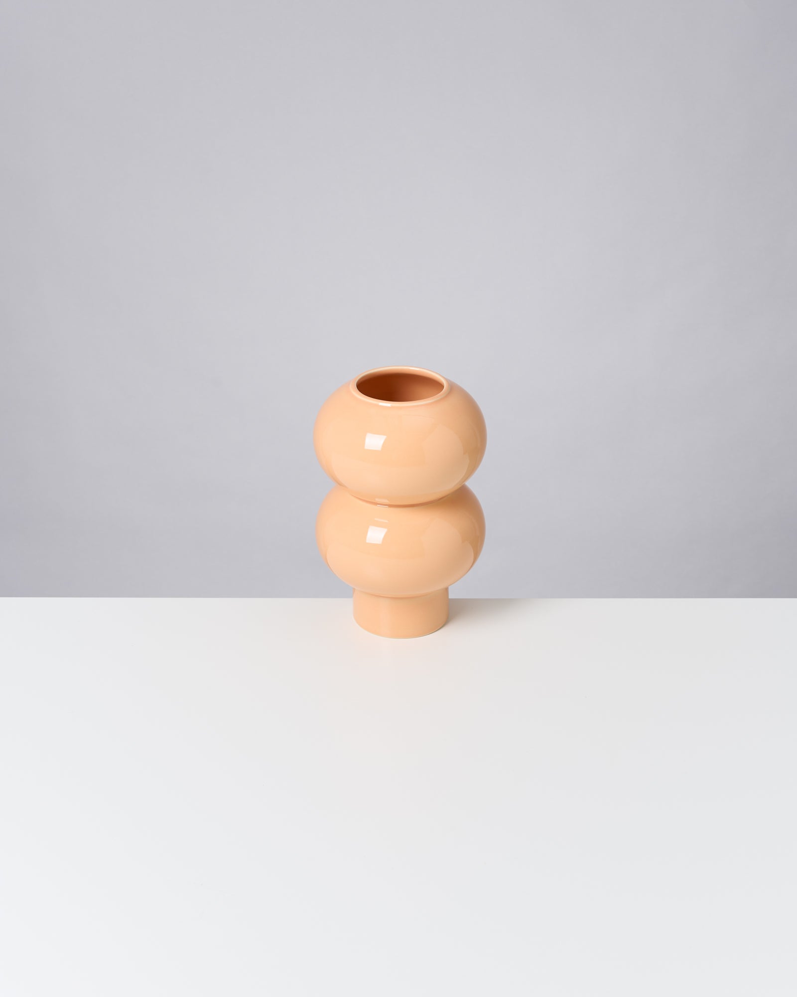Beige, runde Vase mit doppelter Kugelform steht auf weißem Tisch vor grauem Hintergrund.