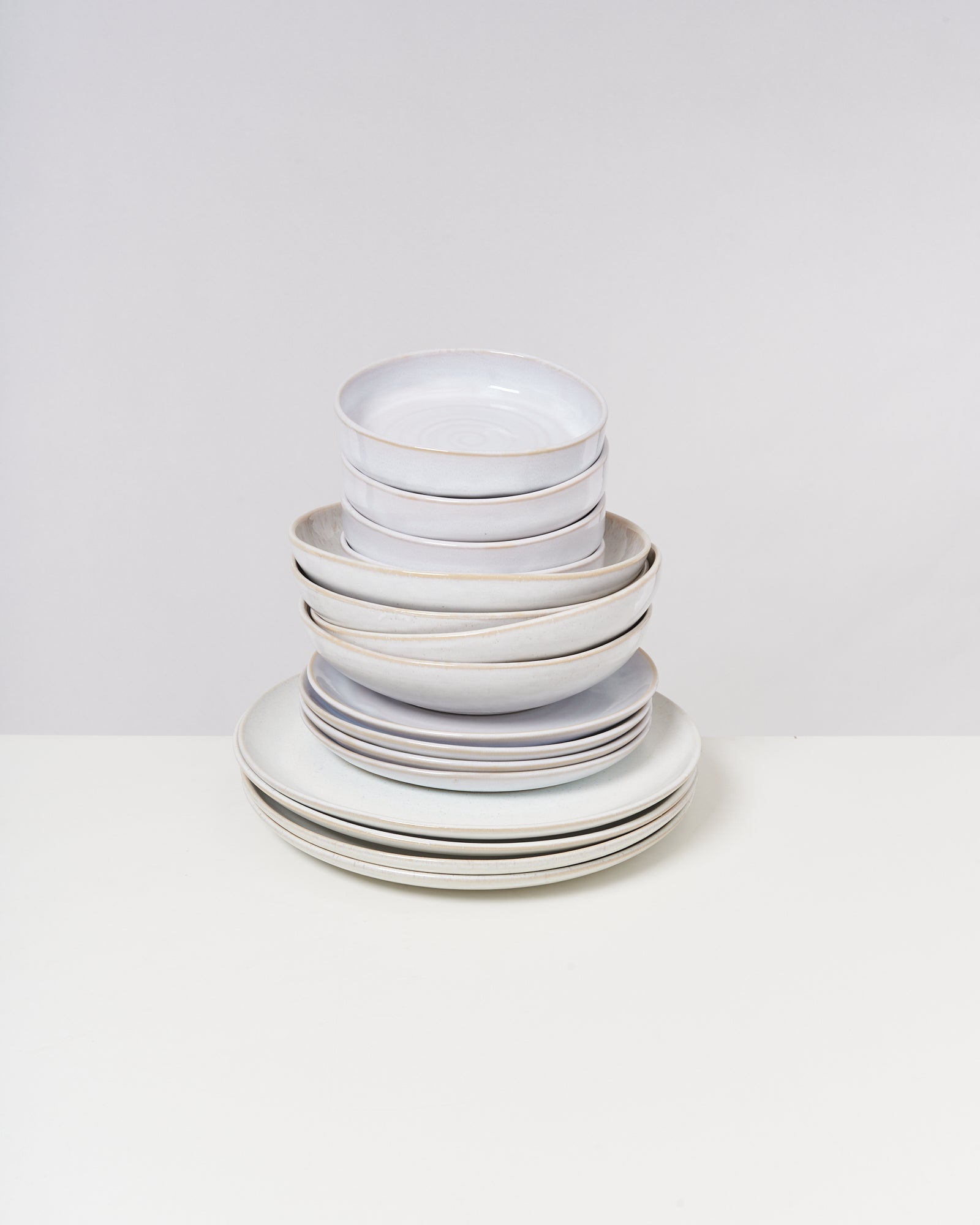 Ein Stapel von weißen, unterschiedlich großen Tellern und Schalen auf einem Tisch vor einem weißen Hintergrund.