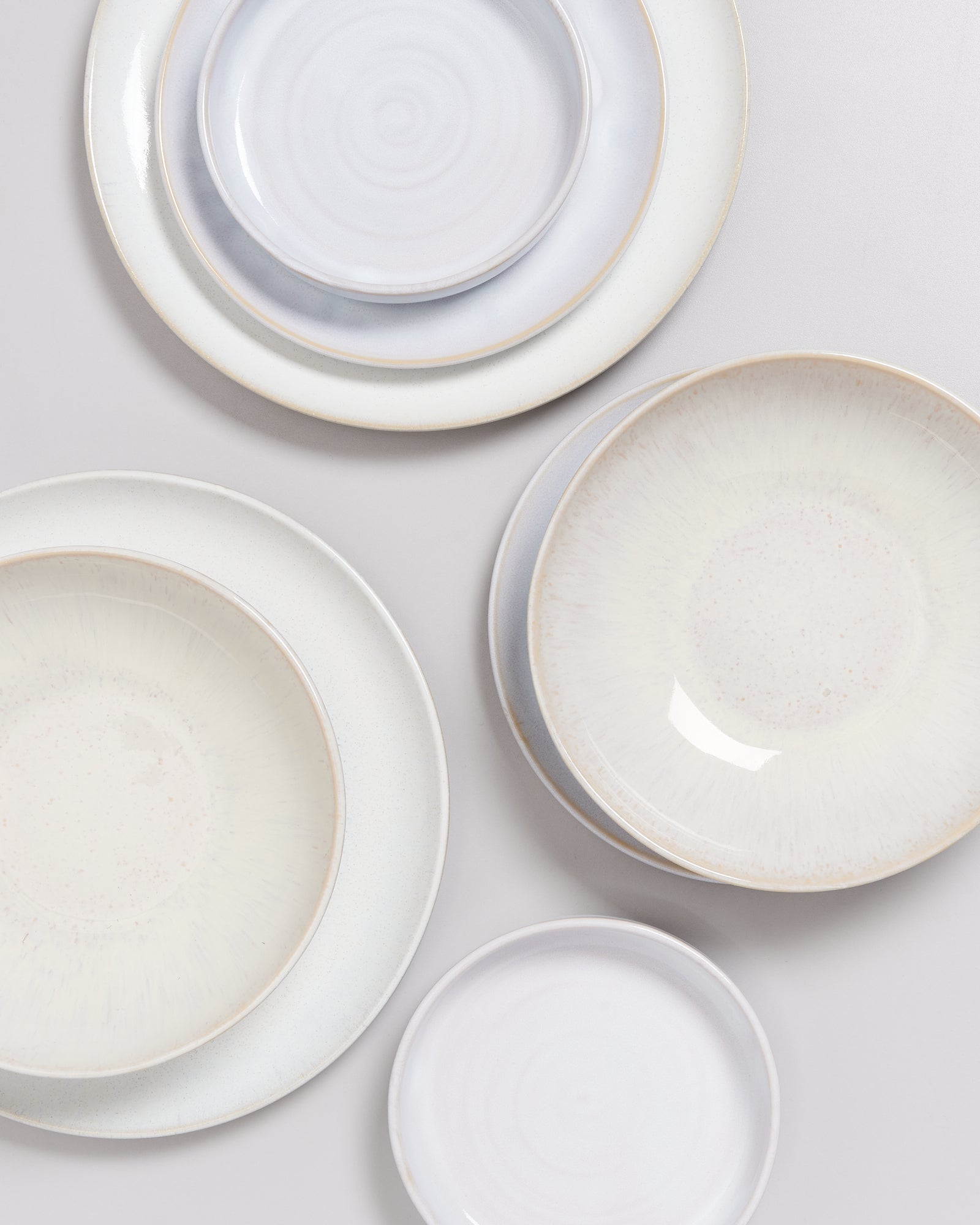 Verschiedene gestapelte Teller in sanften Weiß- und Beigetönen auf einem Tisch.
