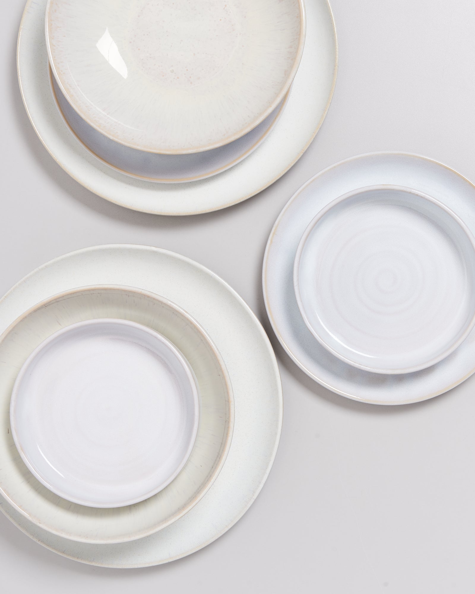 Übereinander gestapelte, runde Keramikteller in hellen Farben auf einer grauen Oberfläche.