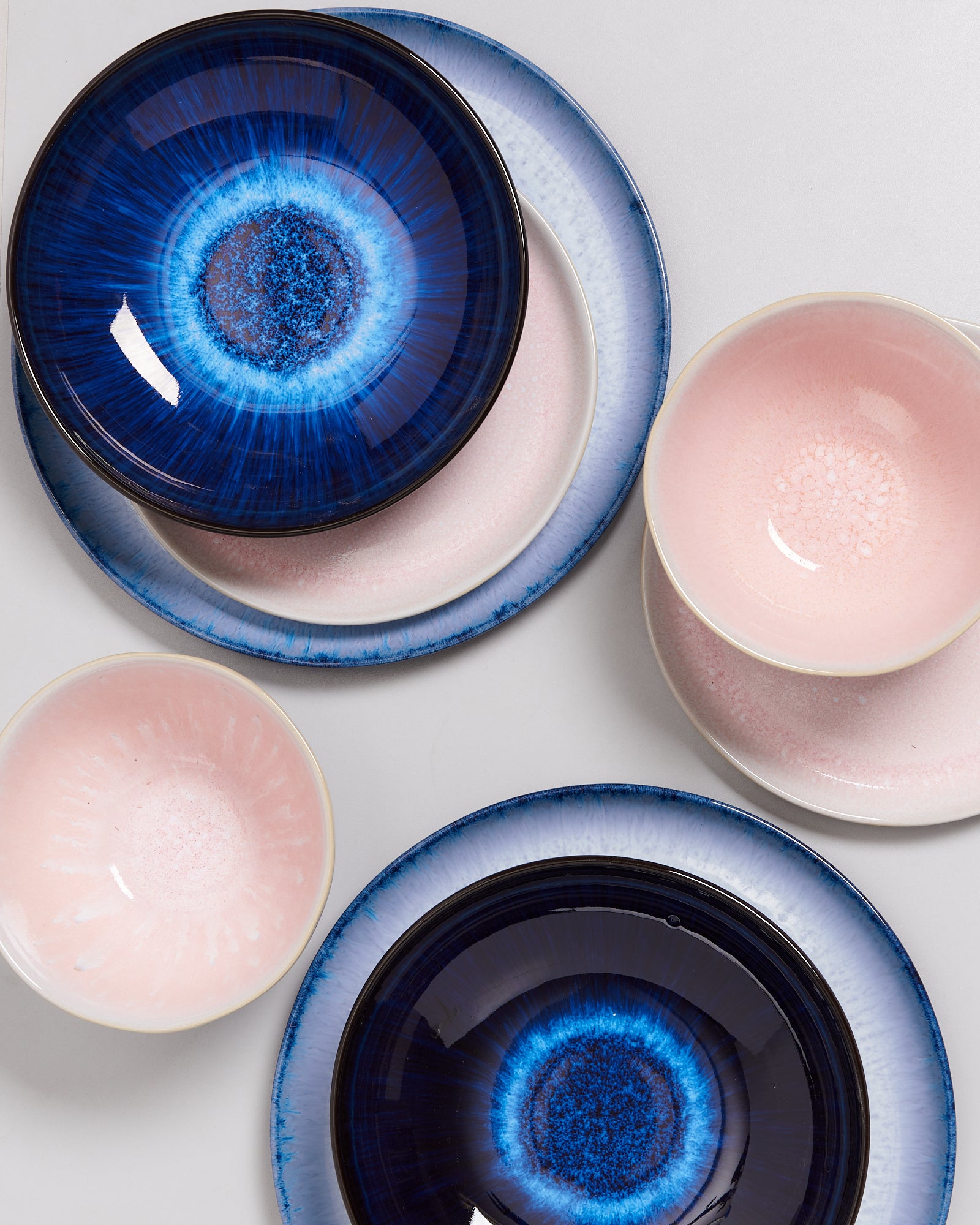 Verschiedene blaue und rosa Keramikteller und Schüsseln mit kunstvollen Designs auf einer hellen Oberfläche.