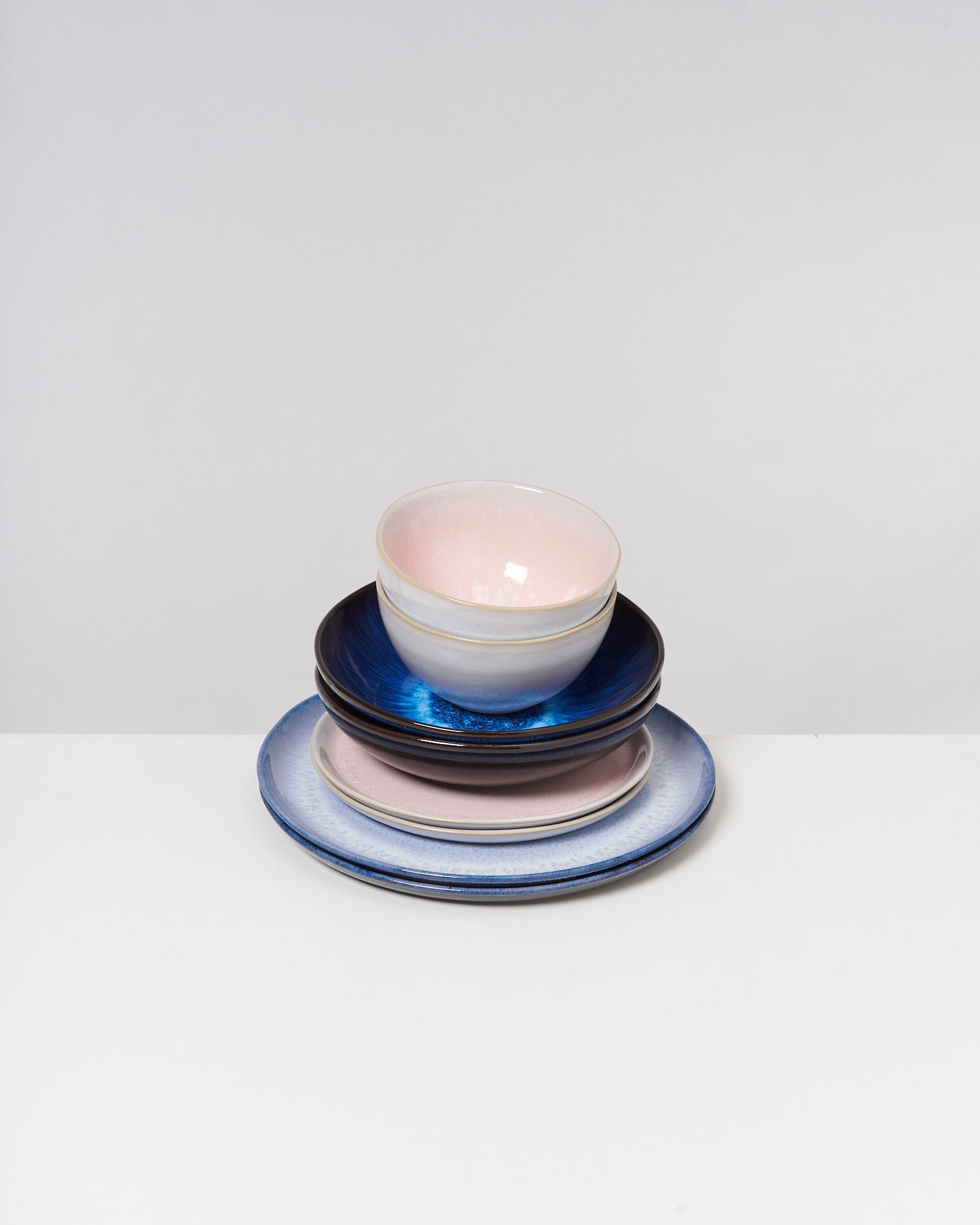 Ein Stapel bunter Keramikteller und -schalen in verschiedenen Farben auf weißem Hintergrund.